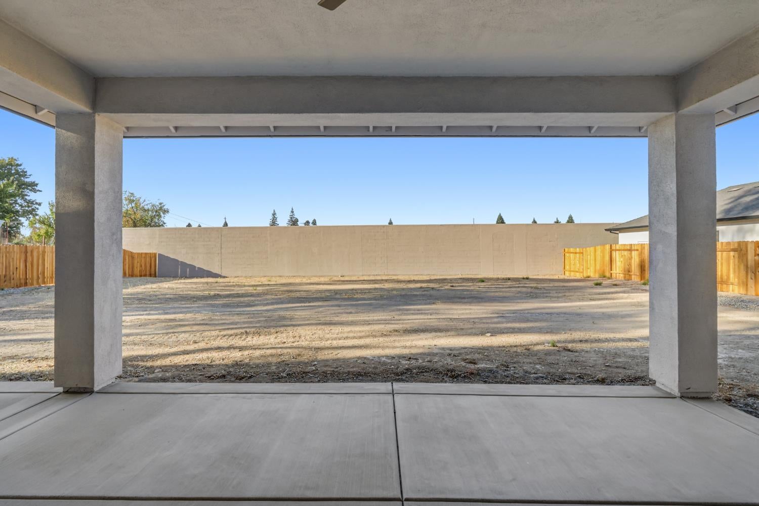 Covered concrete patio overlooking a bare, fenced backyard and tall masonry wall.