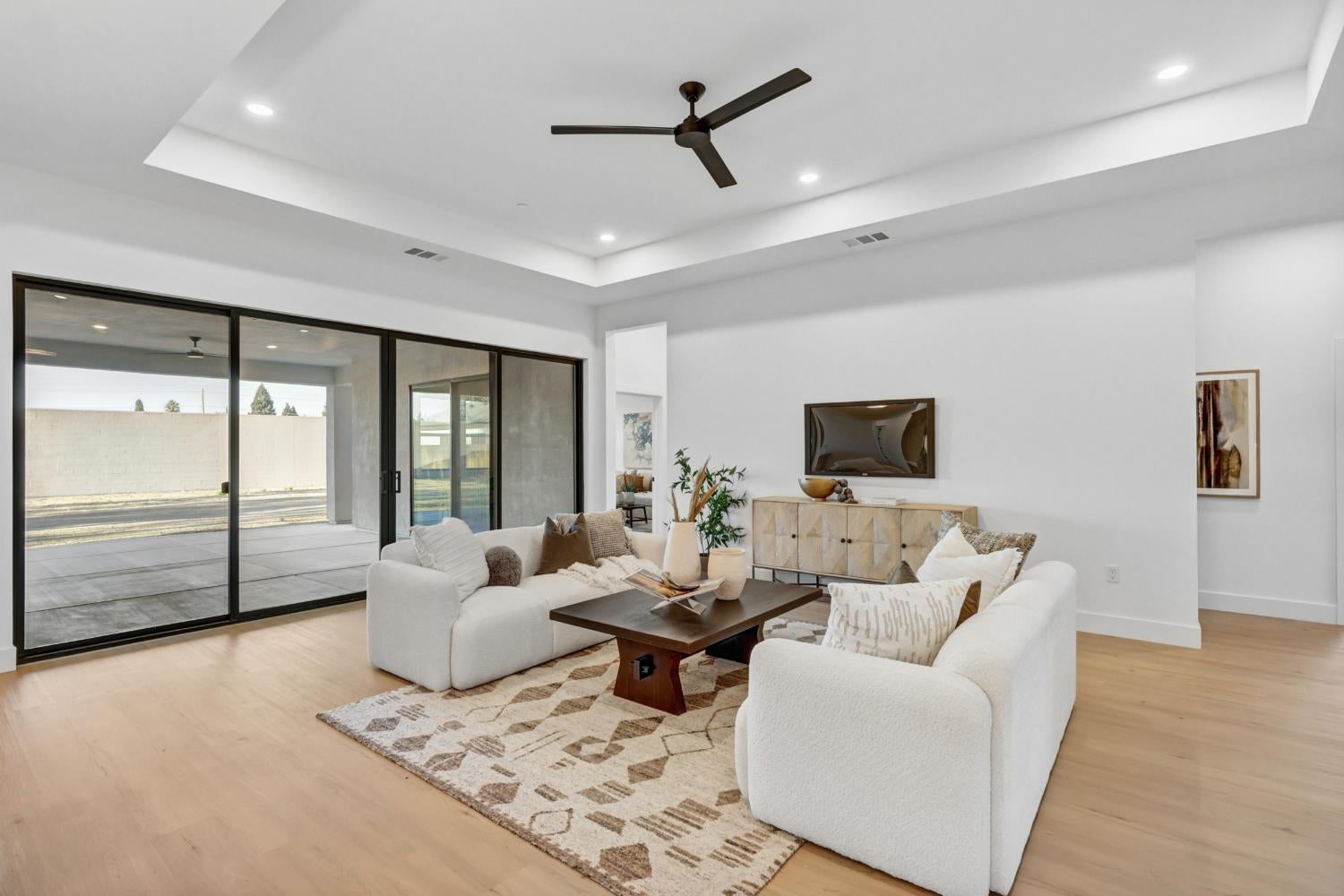 Staged living room with white sofas, a patterned rug, and large sliding glass doors to a covered patio.