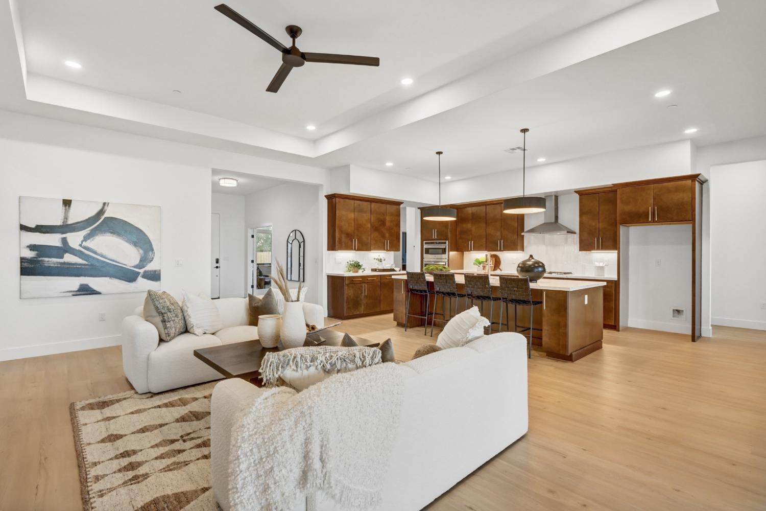 Open-plan living room and kitchen with white sofas, dark wood cabinets, and a large island.