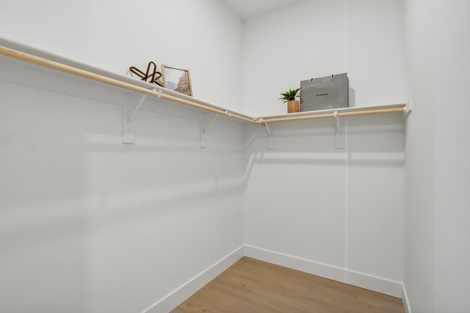 Walk-in closet with wraparound wood hanging rods, upper shelving, and light wood flooring.