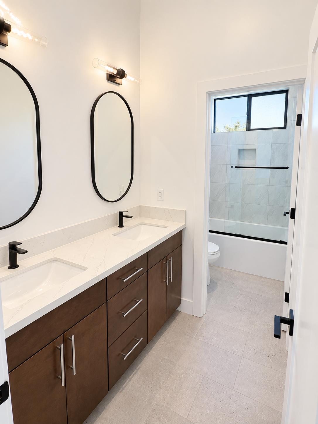 Bathroom with a double vanity, dark wood cabinetry, arched mirrors, and a tiled tub-shower.