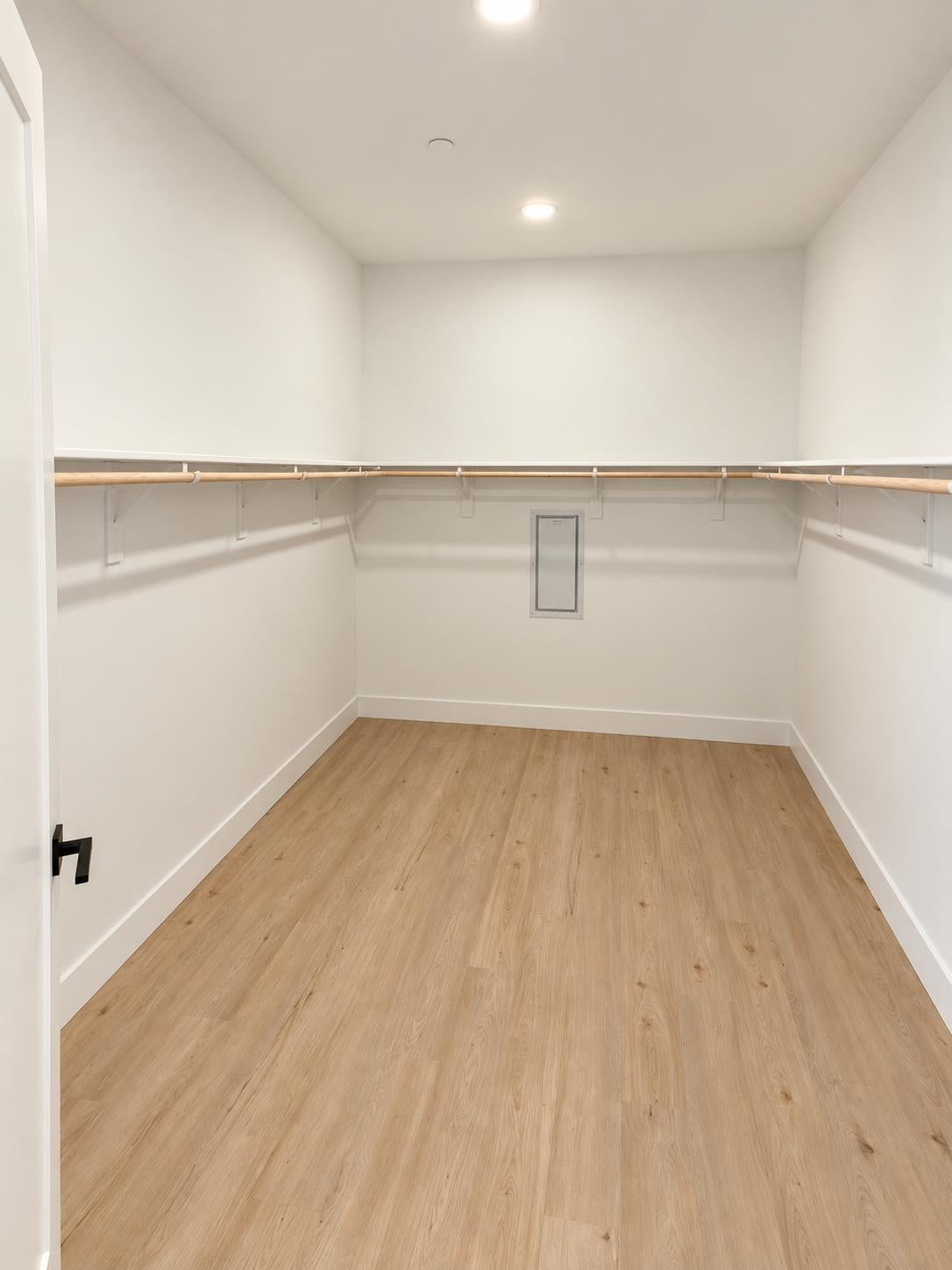 Empty walk-in closet with wood flooring and wraparound hanging rods and shelves.