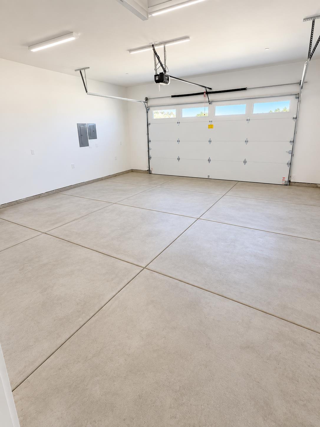 Empty garage with a sectional overhead door, narrow windows, and a light-colored tiled floor.