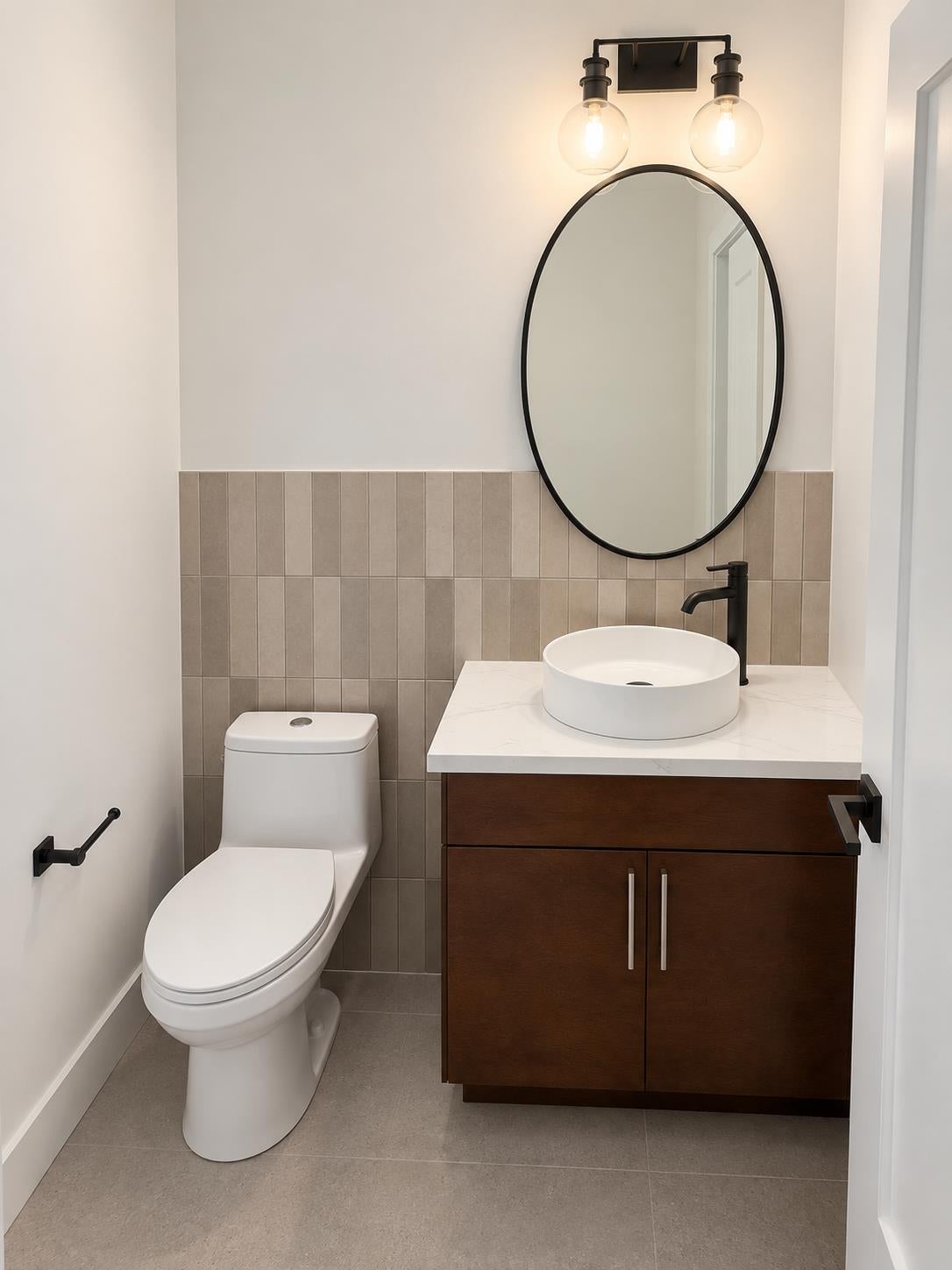 Bathroom with a dark wood vanity, vessel sink, oval mirror, and vertical beige tile.