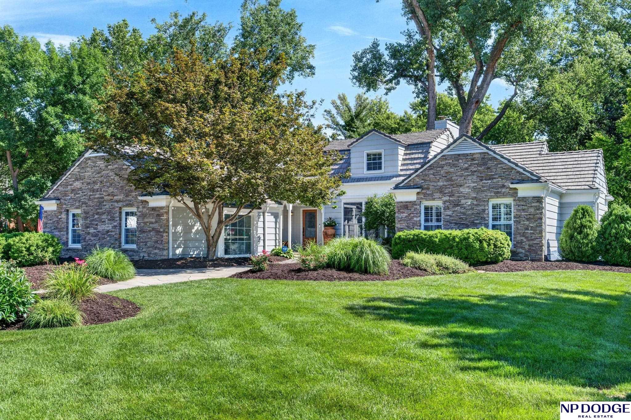 Two-story home with stone gables, light siding, and a landscaped lawn beneath mature trees.