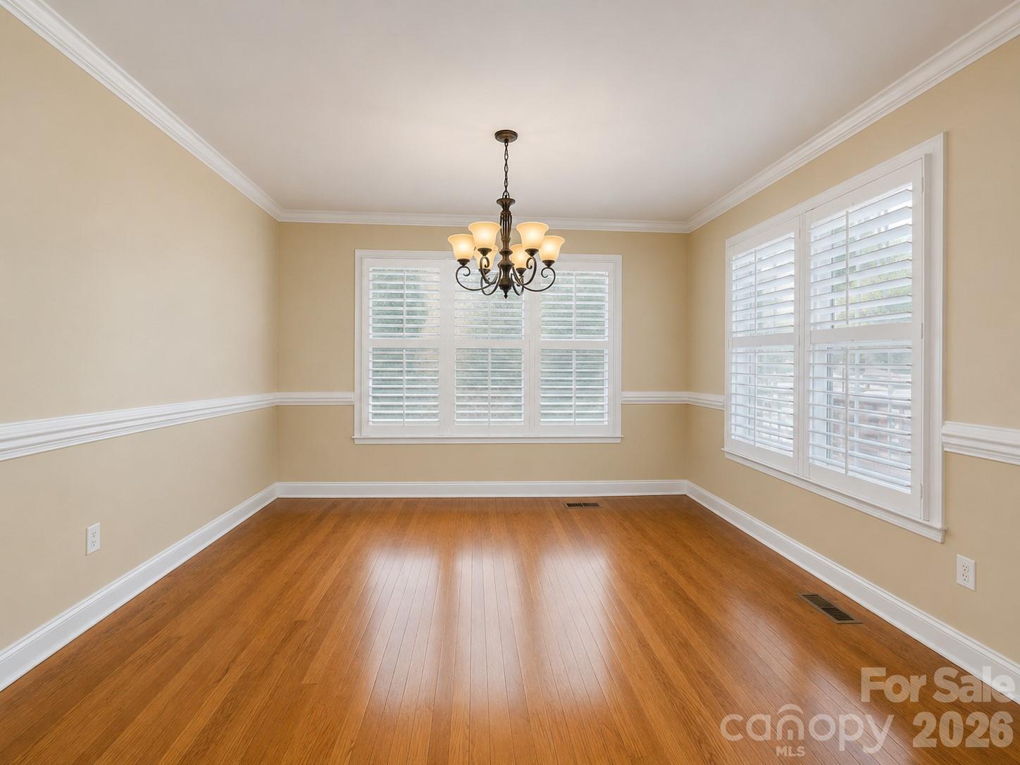 Empty dining room with hardwood floors, plantation shutters, and a lit chandelier.