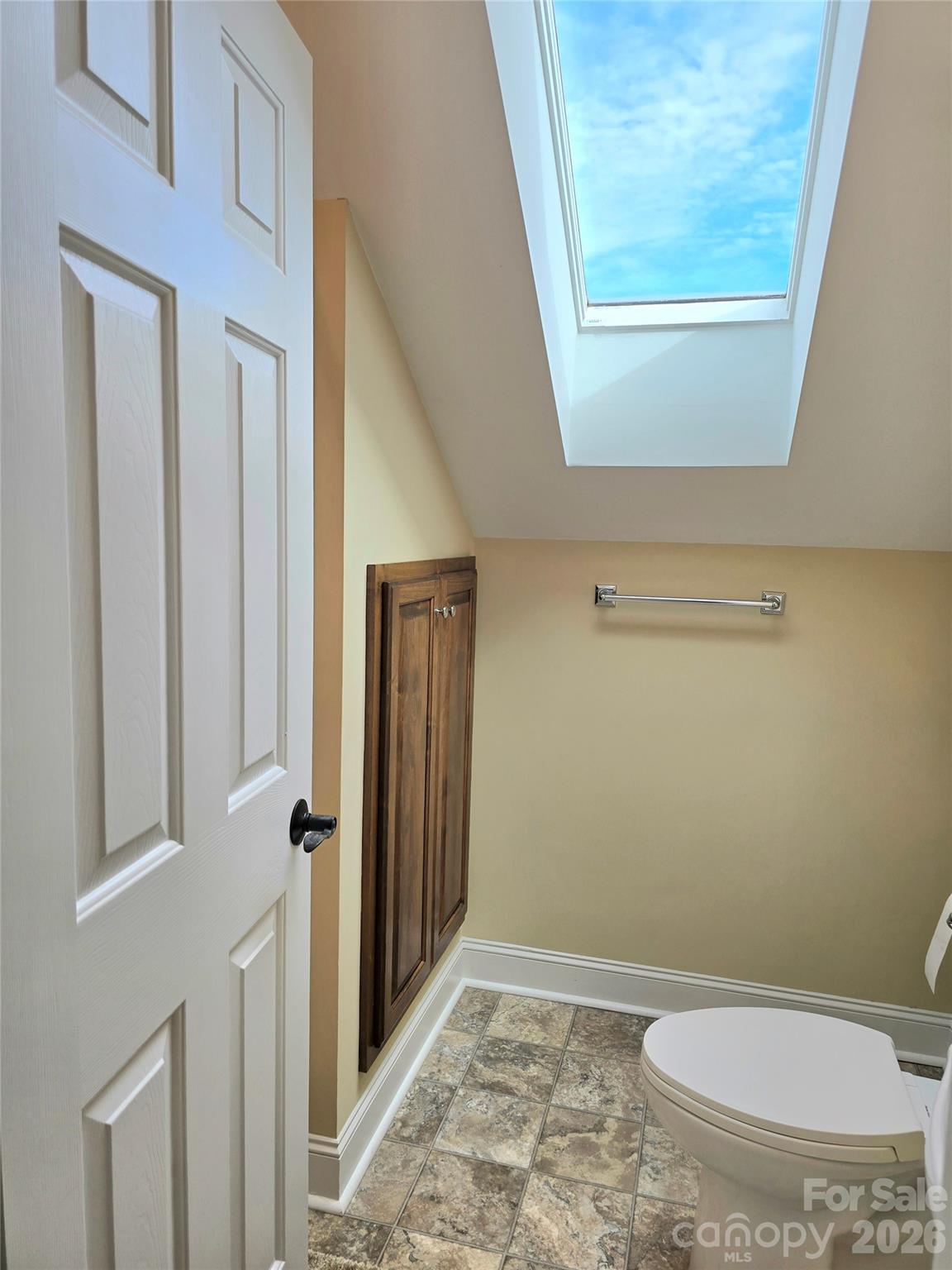 Bathroom with a large skylight, dark wood wall cabinet, and mottled tile floor.