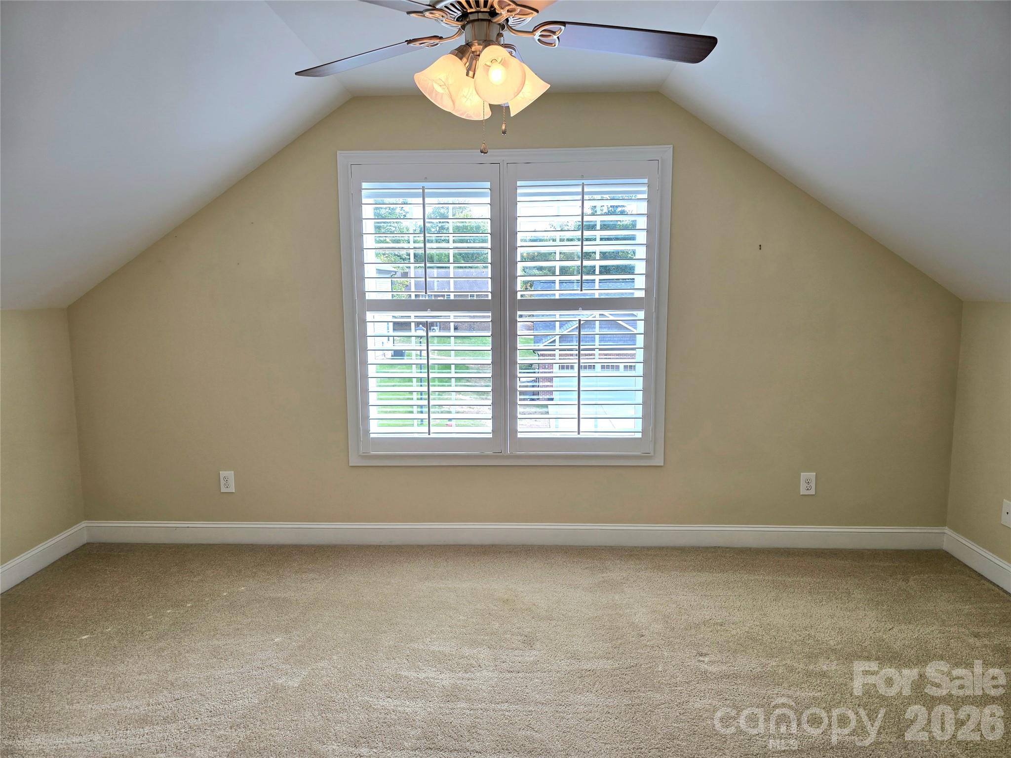 Vacant carpeted bedroom with a vaulted ceiling, ceiling fan, and shuttered windows.