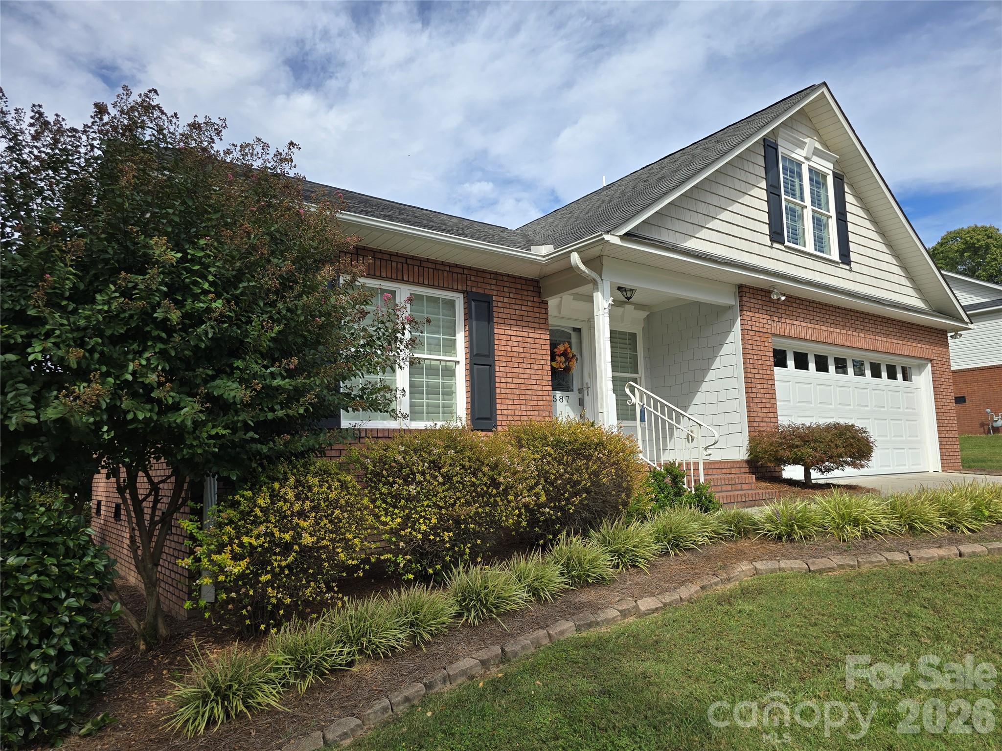 Brick-and-shingle home with a steep gabled roof, white garage door, and landscaped front yard.