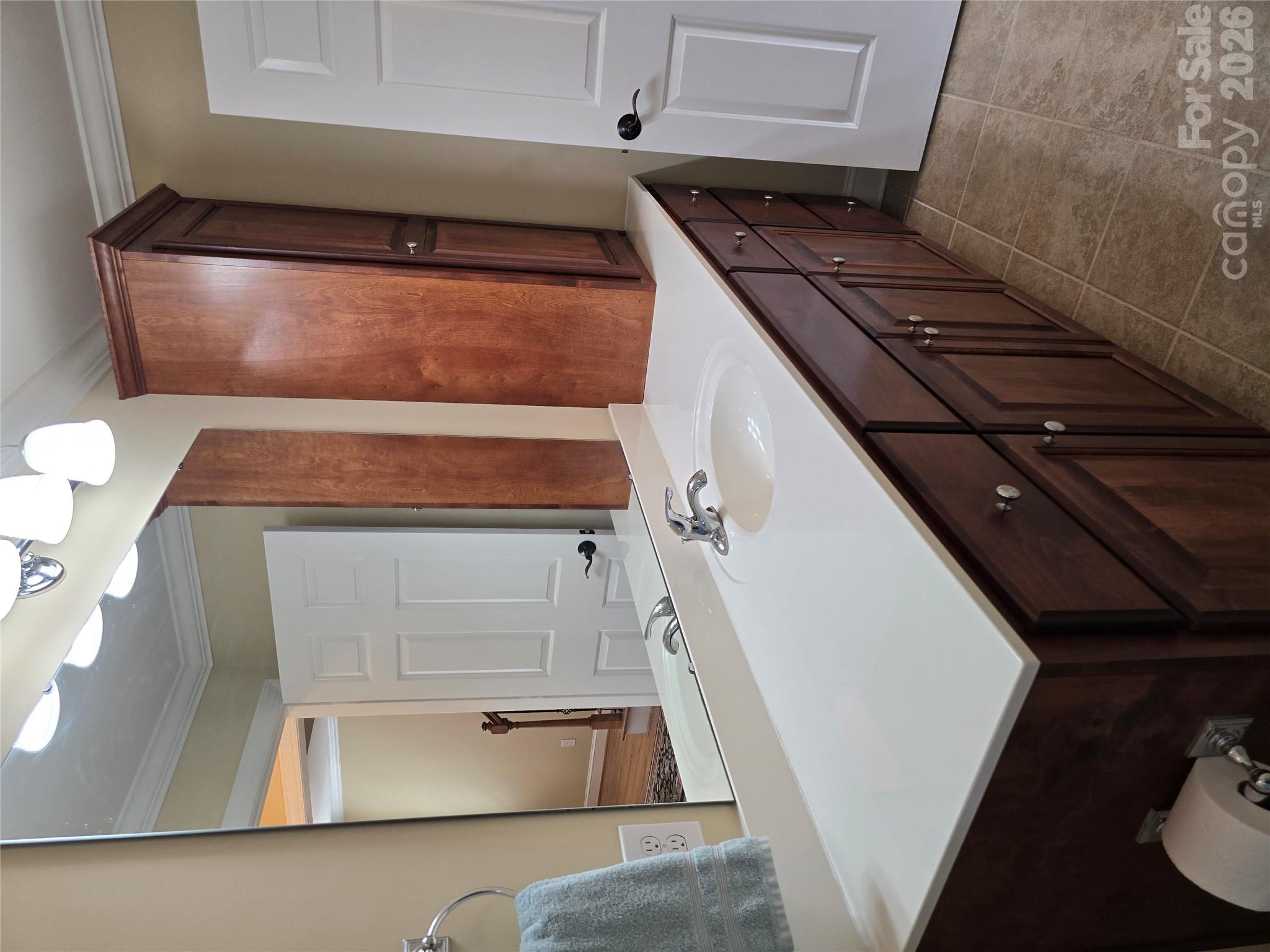 Bathroom with a long white vanity countertop, inset sink, and dark wood cabinets.
