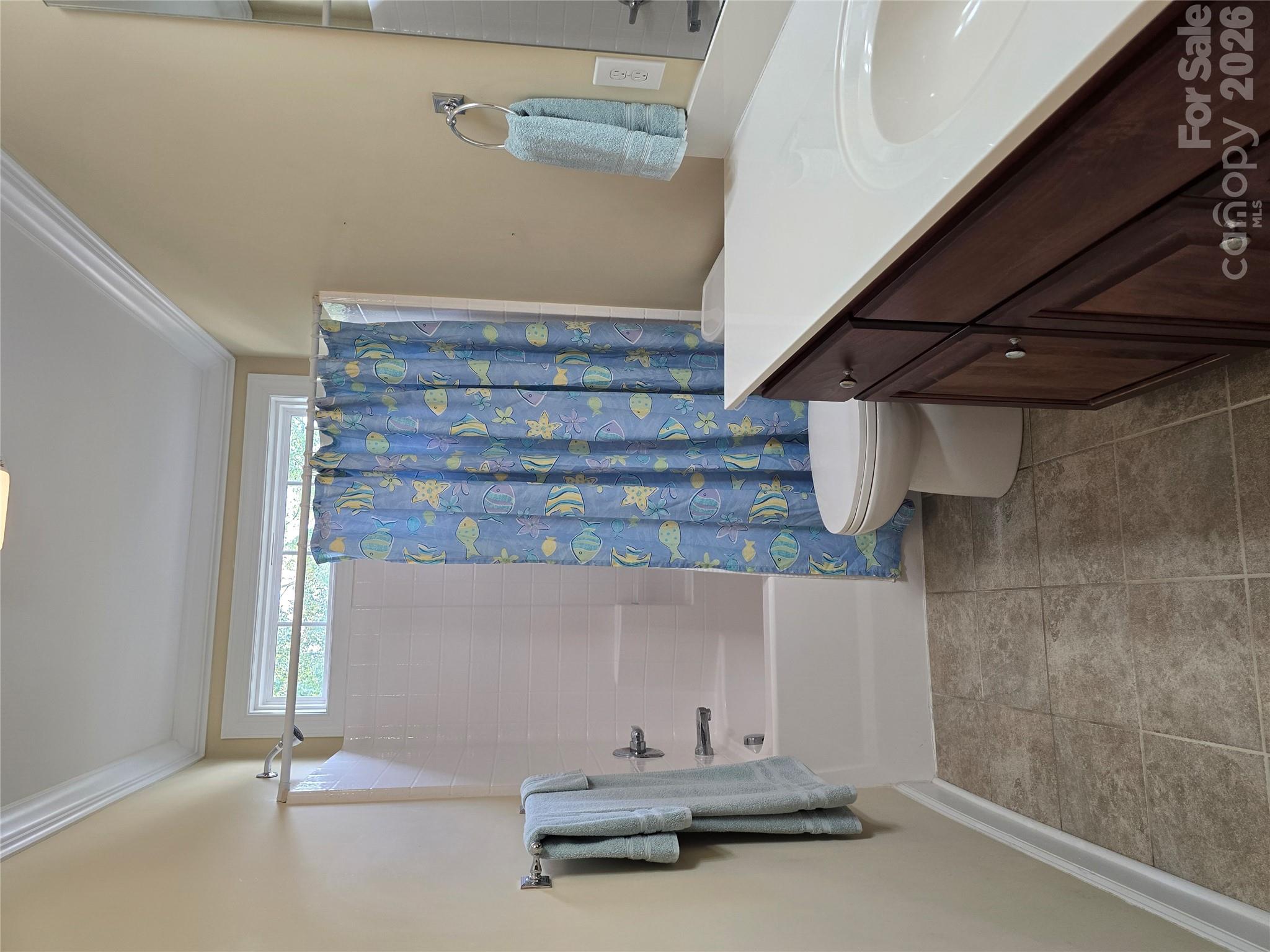 Bathroom with a fish-patterned shower curtain, tiled tub surround, and dark wood vanity.