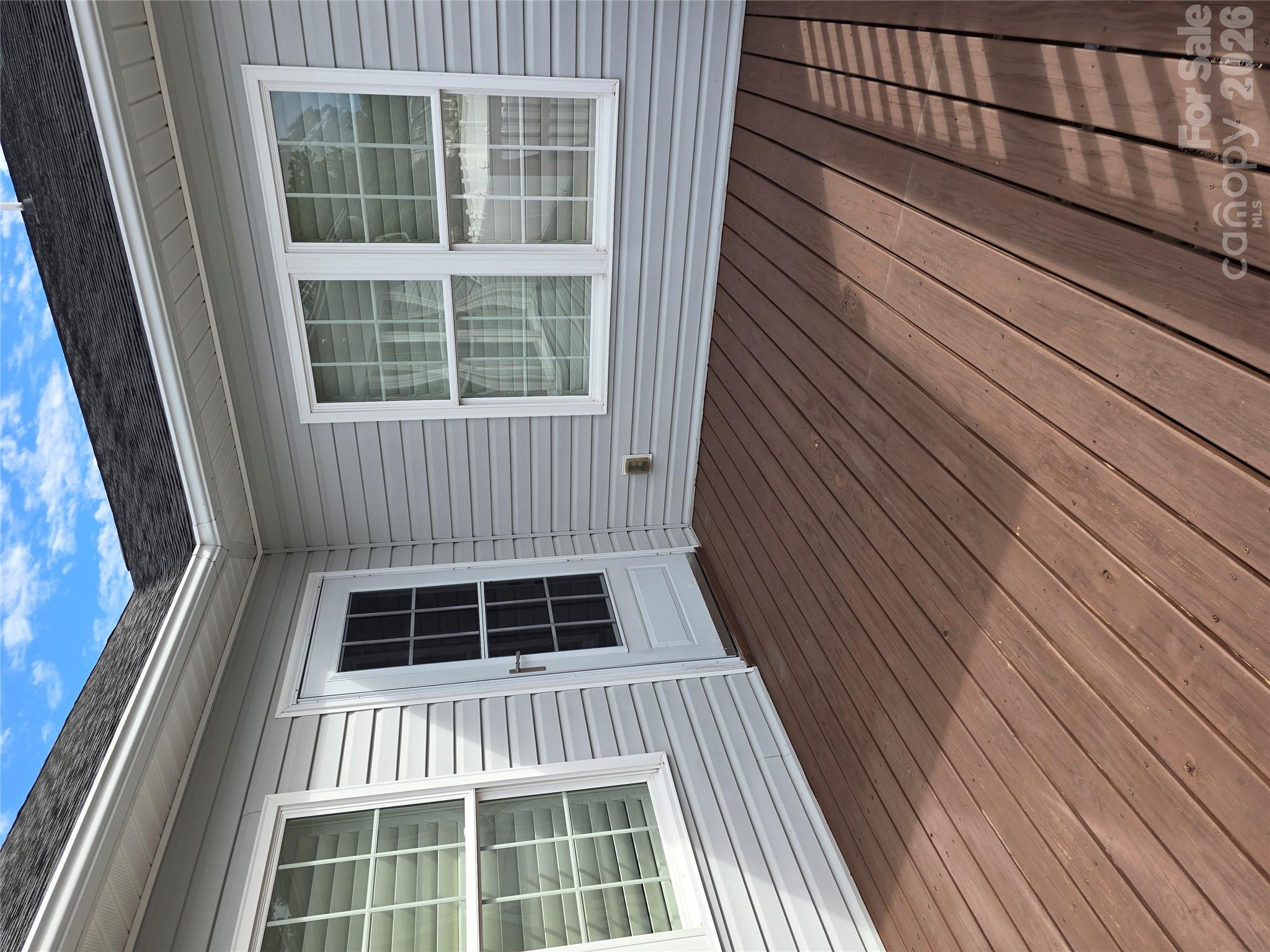 Brown-plank deck beside a gray-sided house, with white-trimmed windows and a glass-paneled door.