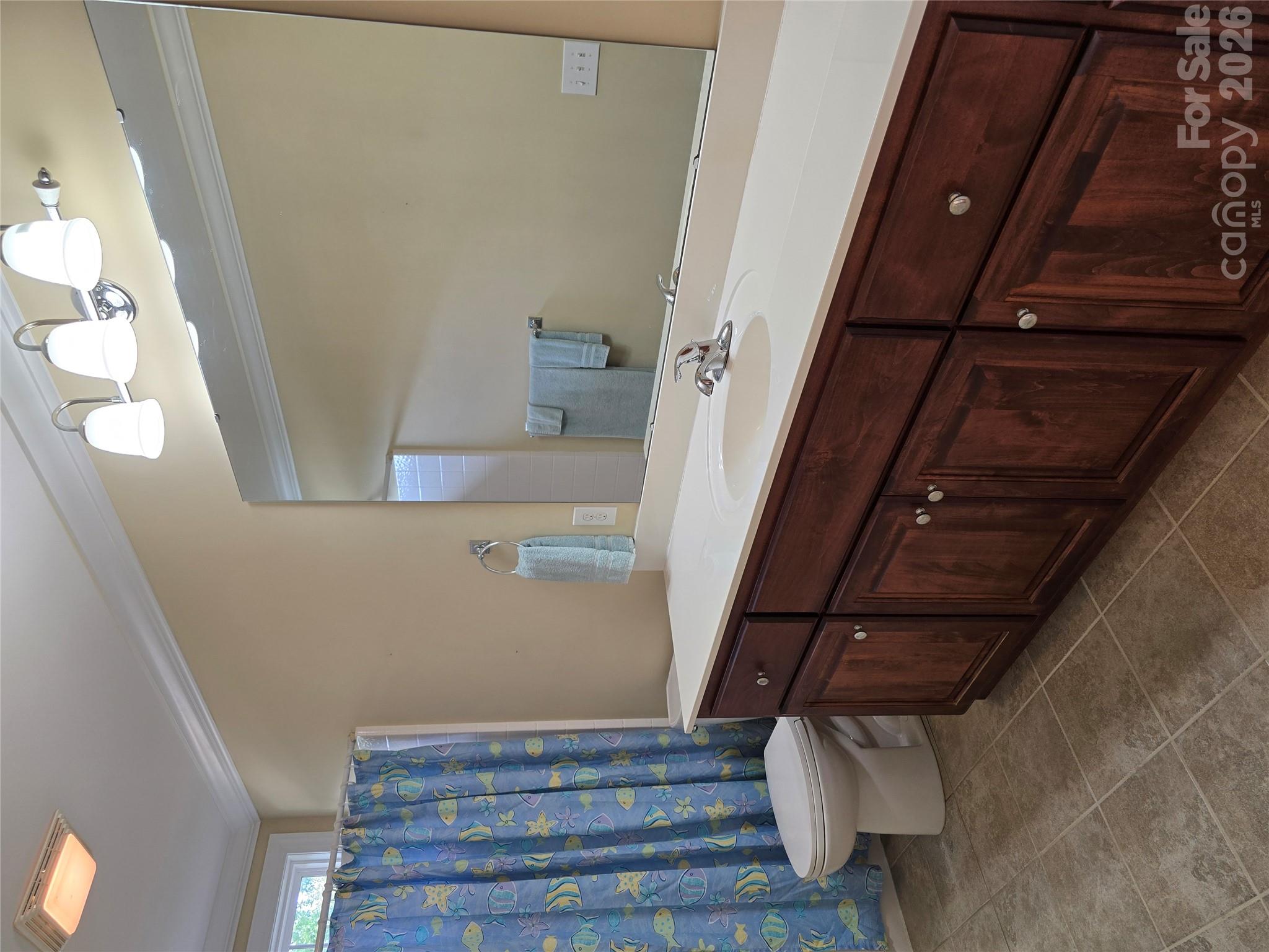 Bathroom with a long dark wood vanity, large mirror, and blue fish-pattern shower curtain.