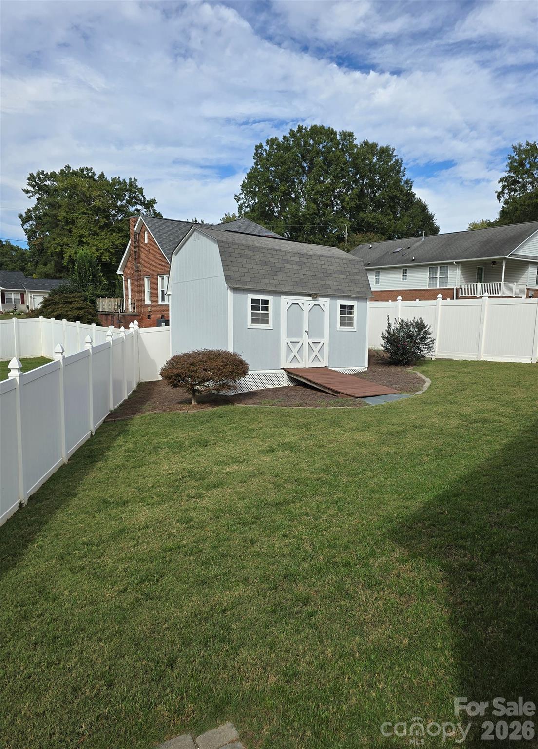 Backyard shed with white trim and a wooden ramp, surrounded by a white fence and green lawn.