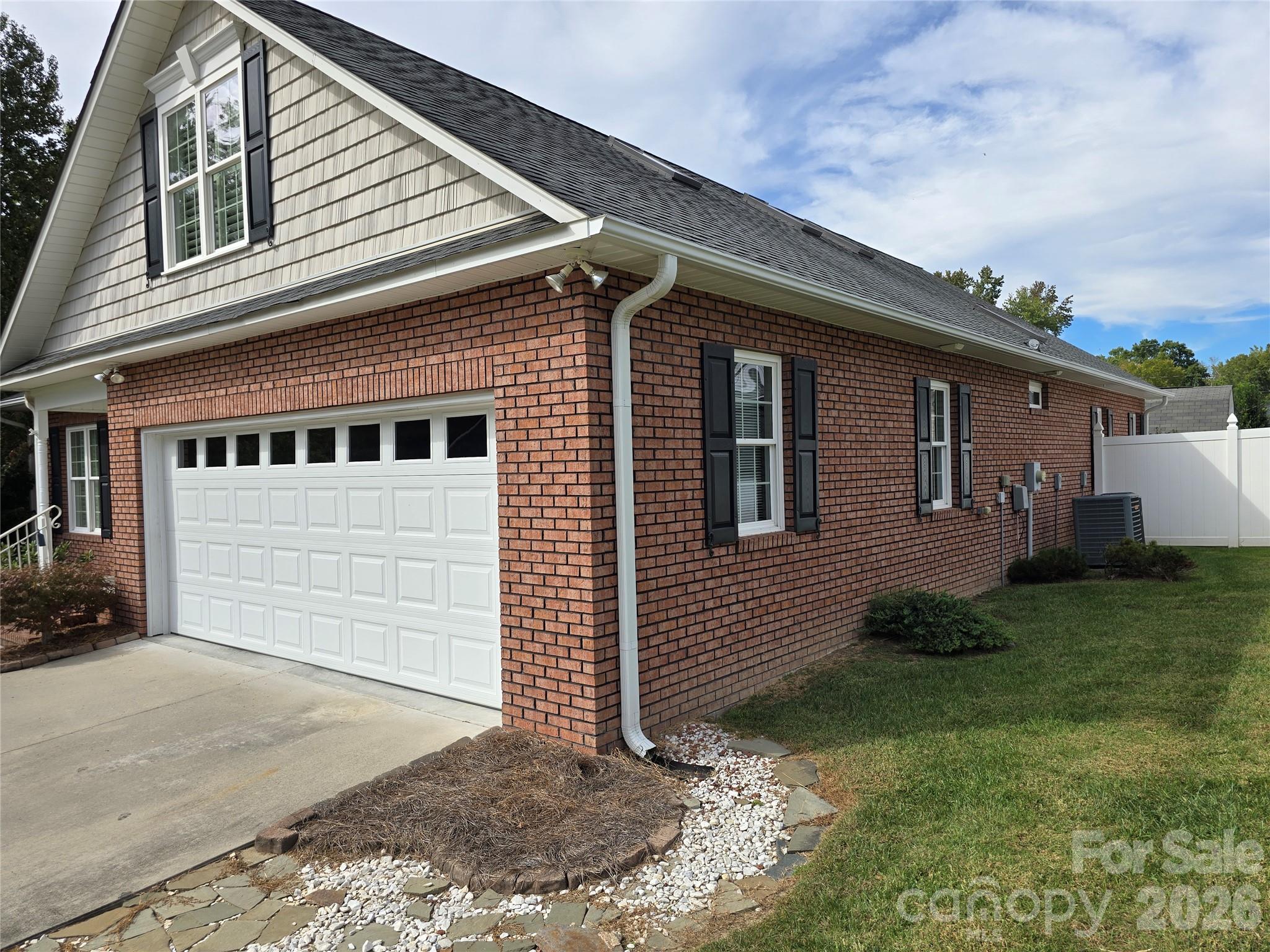 Brick house exterior with a white garage, dormer, black shutters, and a stone-edged lawn.