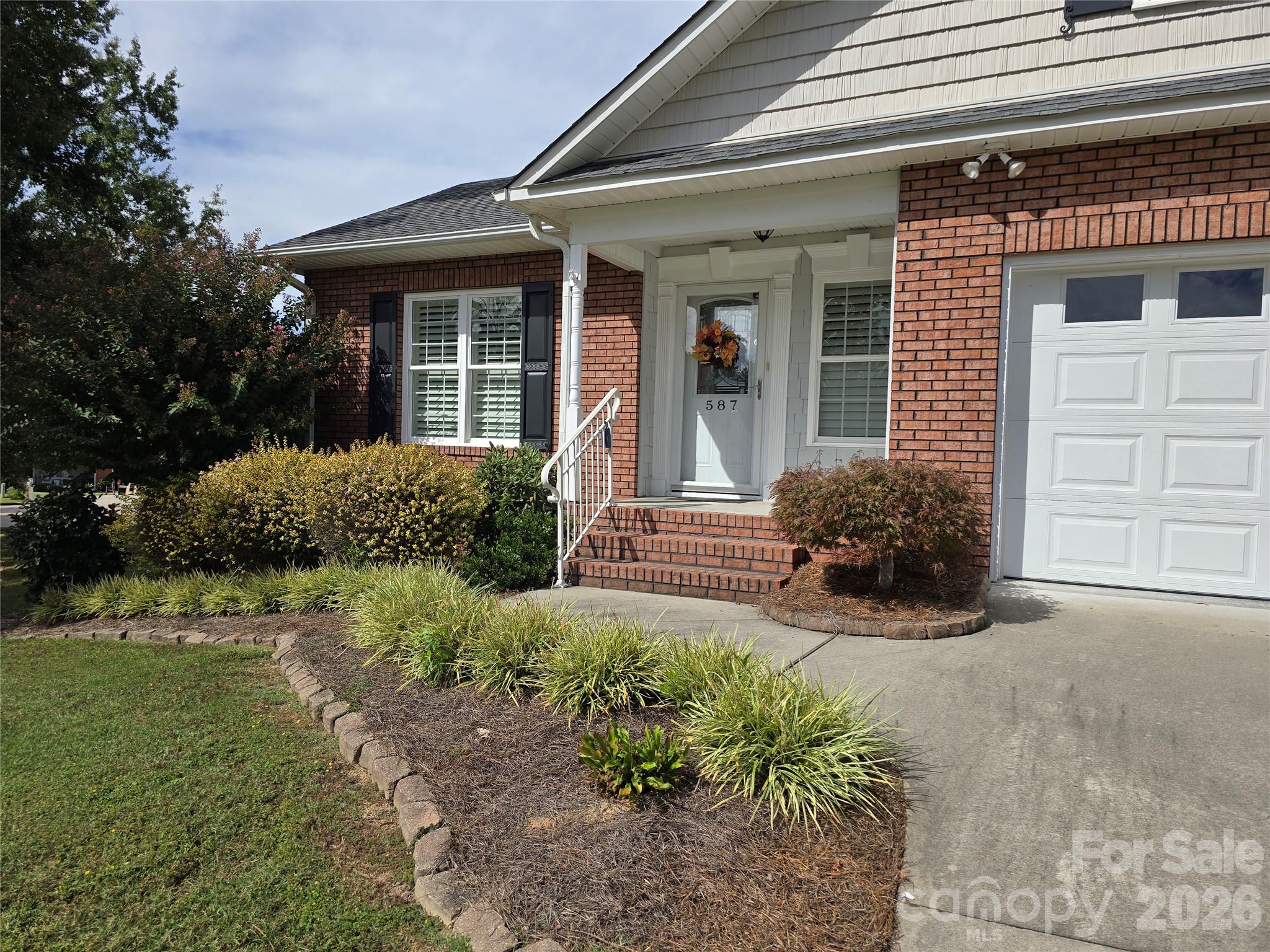 Brick home entrance with white trim, brick steps, landscaped beds, and the number 587 on the front door.