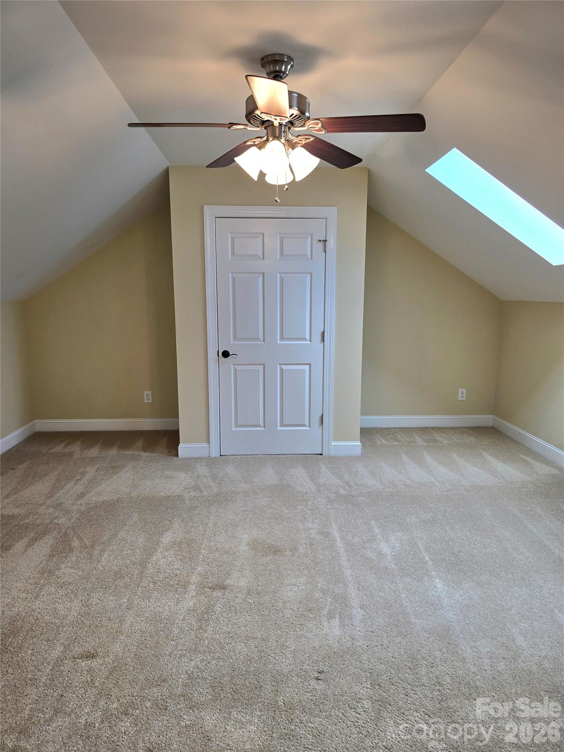 Empty carpeted room with sloped ceilings, a skylight, and a ceiling fan.
