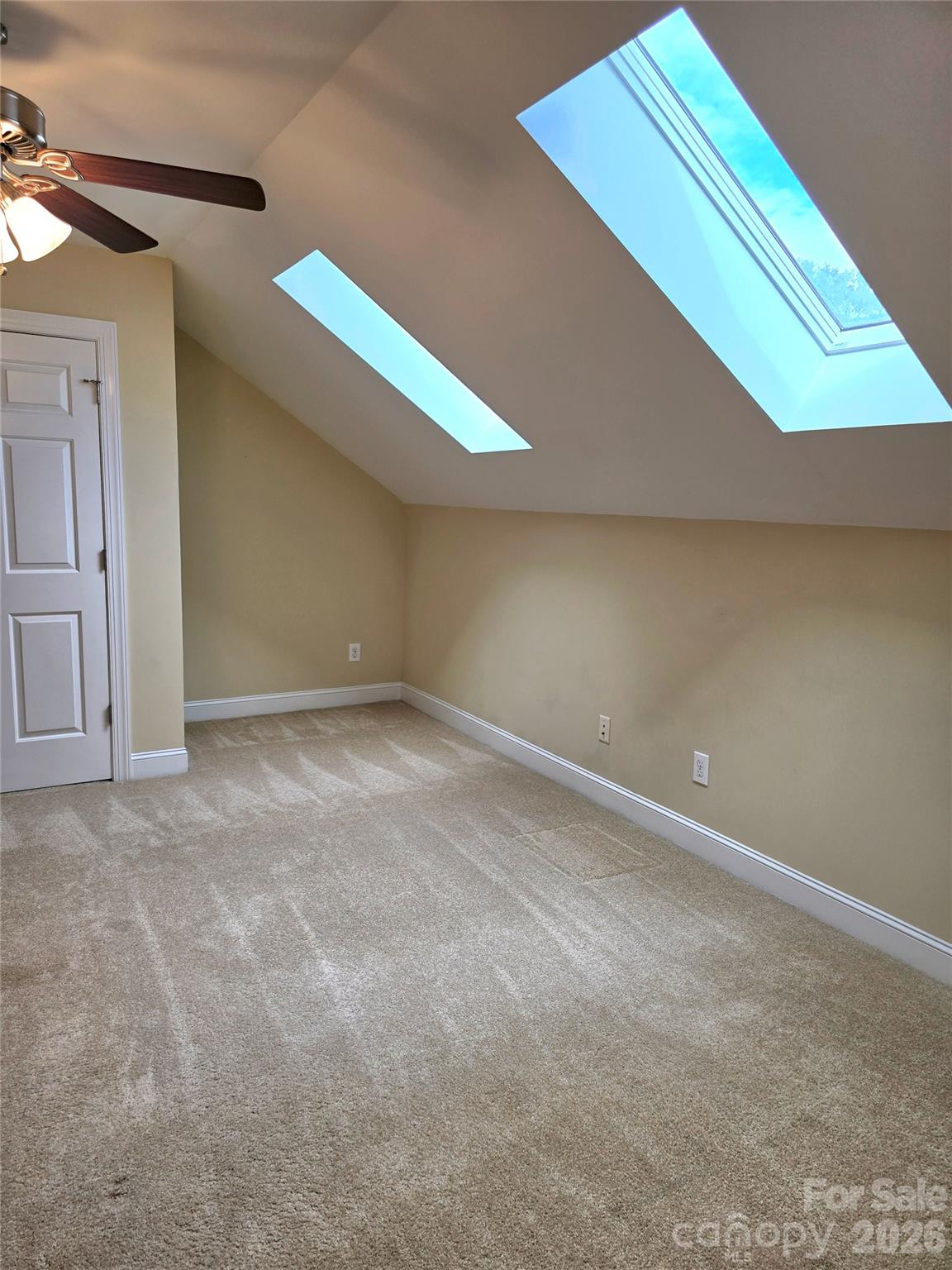 Empty carpeted bedroom with two skylights set into its sloped ceiling.