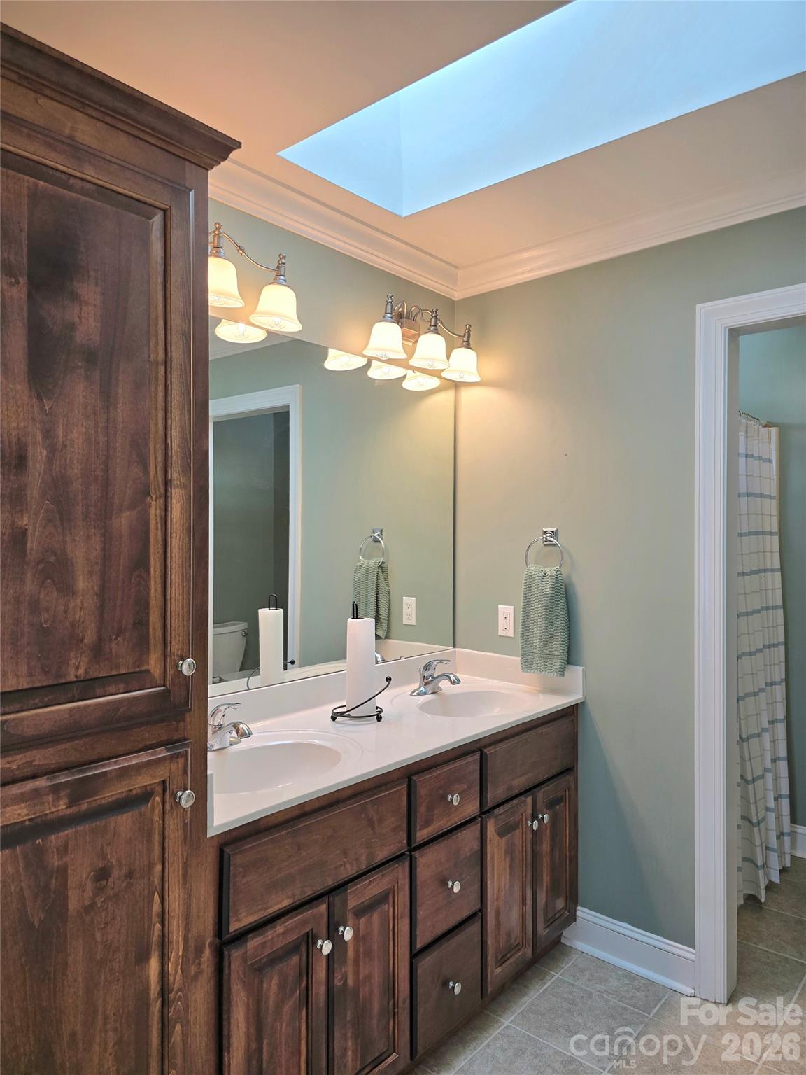 Bathroom with a dark wood double vanity, two sinks, a large mirror, and a skylight.