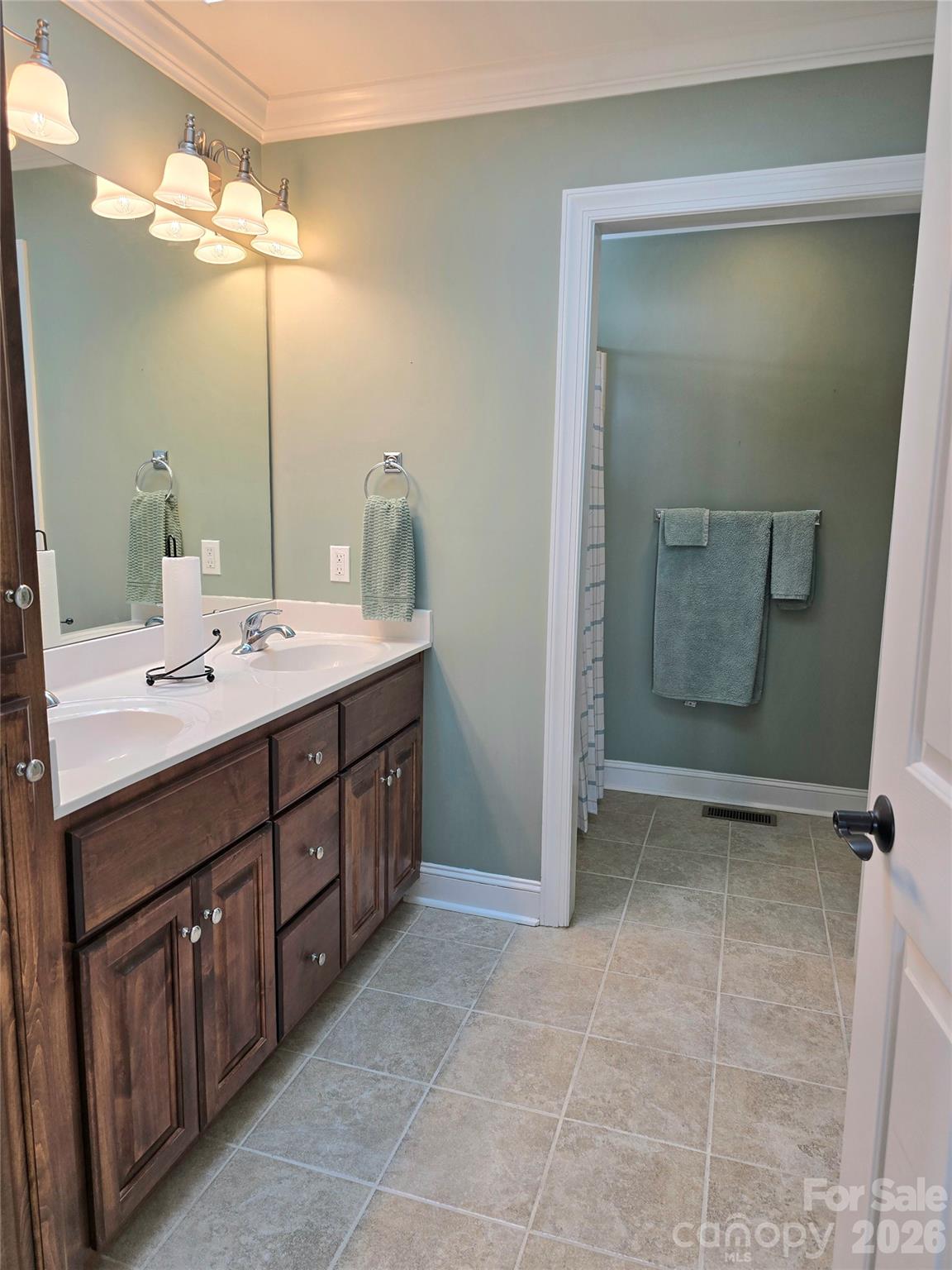 Bathroom with a dark wood double vanity, large mirror, and tiled floor adjoining a towel-lined shower area.