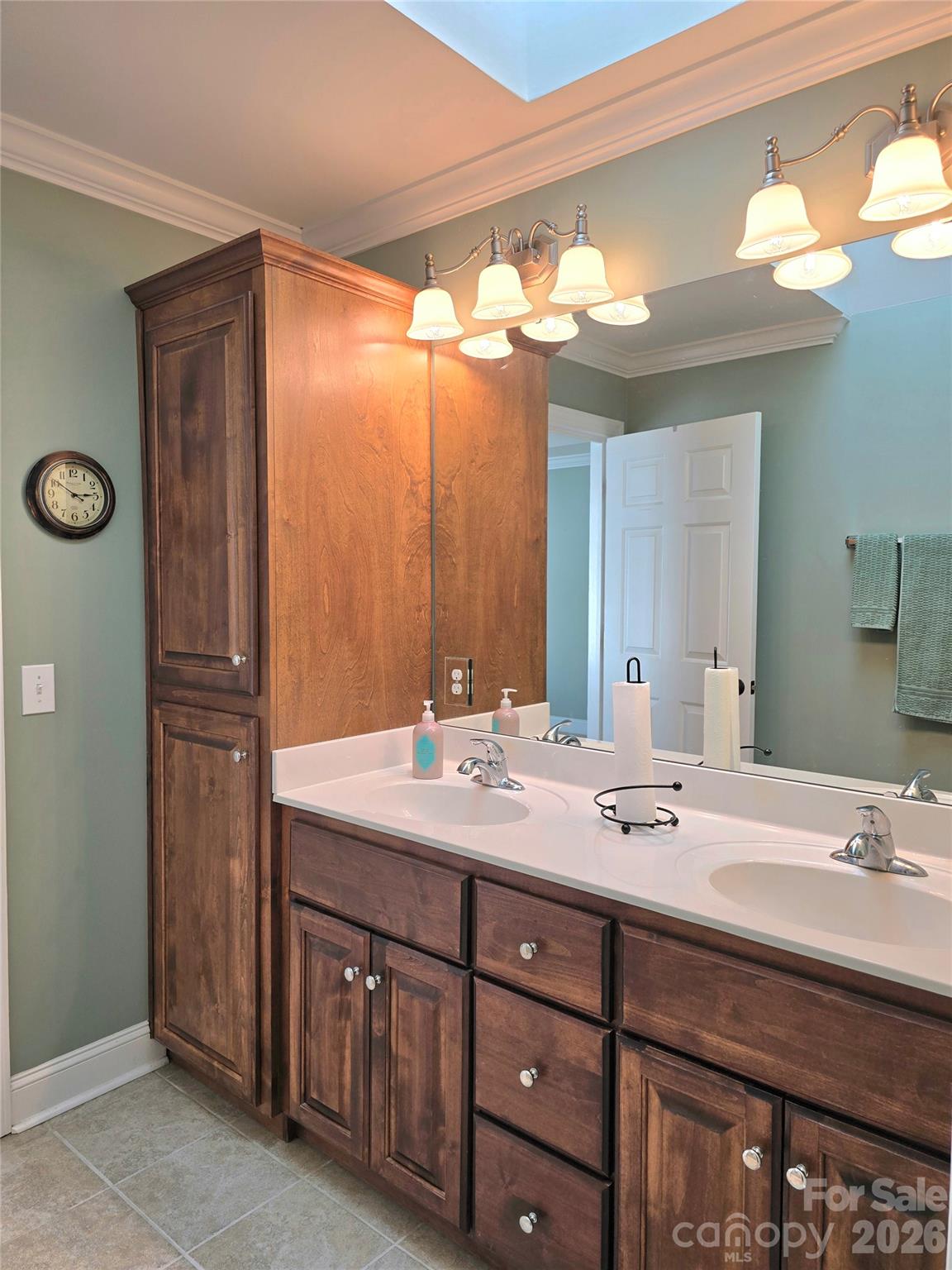 Bathroom with a double-sink vanity, dark wood cabinetry, large mirror, and skylight.