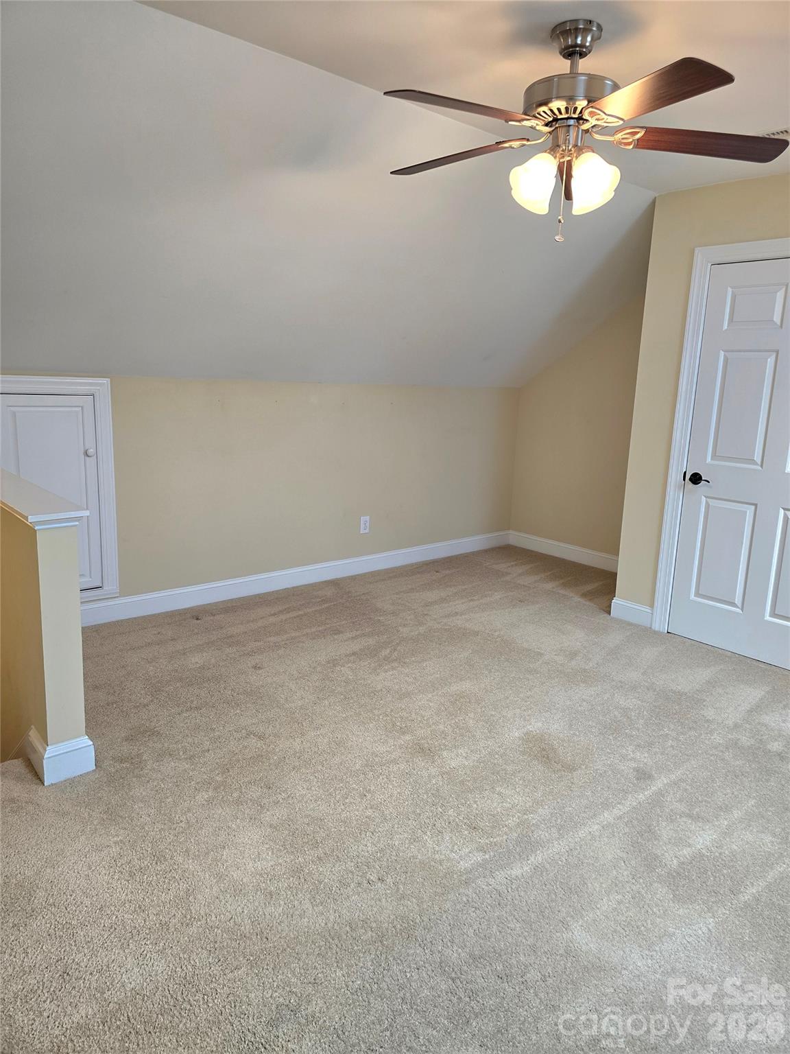 Empty carpeted room with a sloped ceiling, ceiling fan, and small built-in access door.