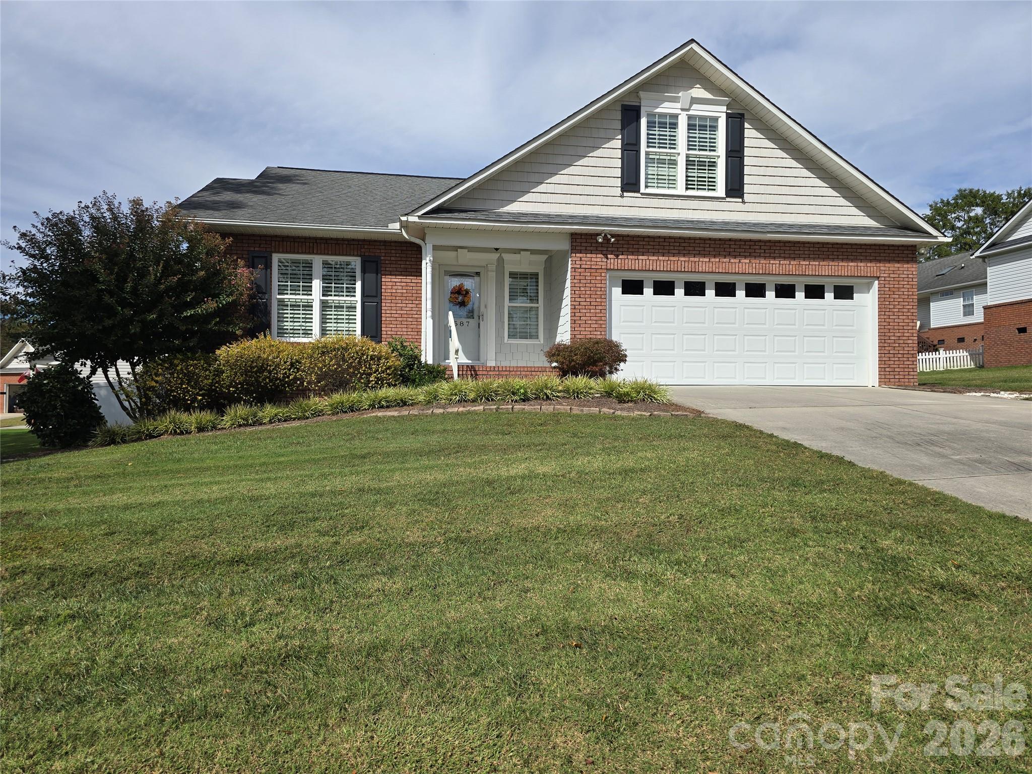 Brick house with a white gable, black shutters, attached garage, and landscaped front lawn.