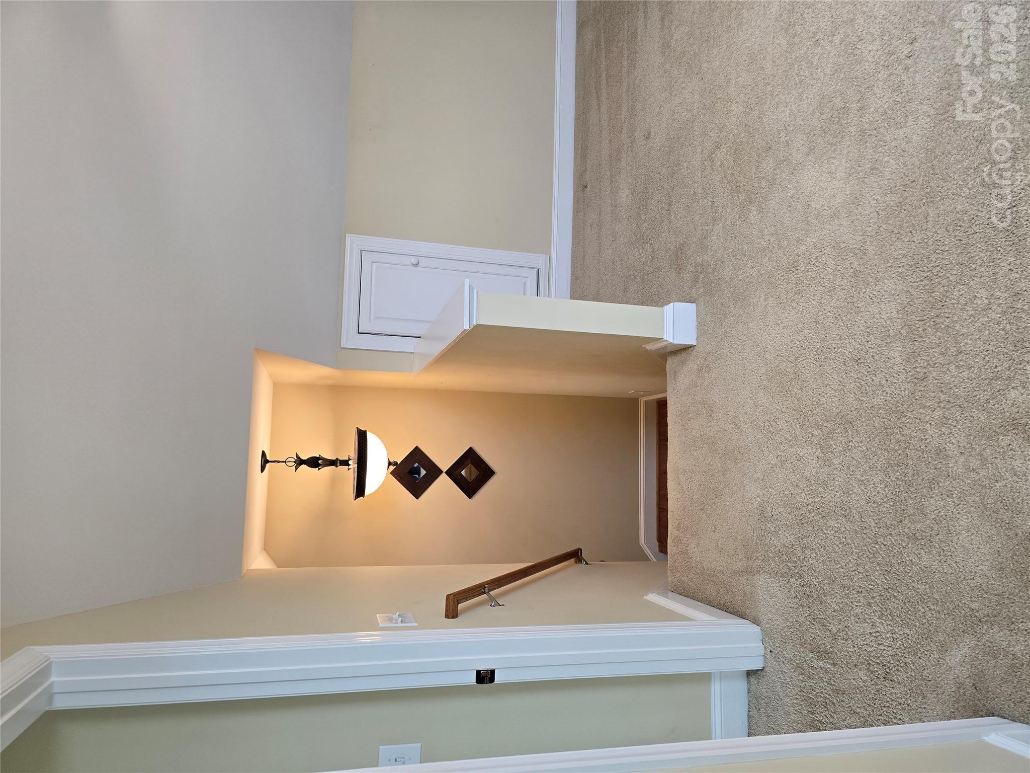 Upstairs landing with a carpeted floor, open stairwell, wooden handrail and hanging light.