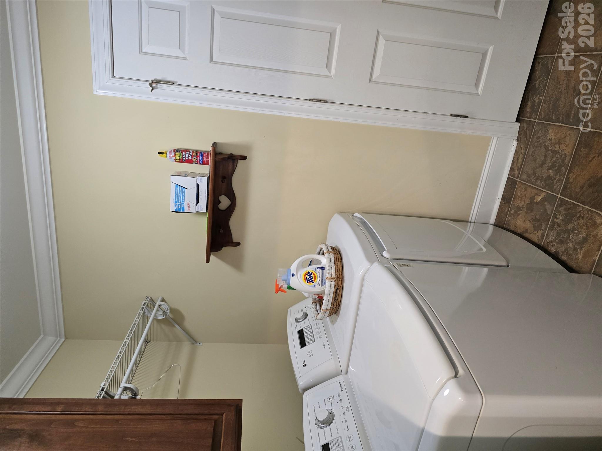 Laundry room with white washer and dryer, wire shelving, and brown tile flooring.