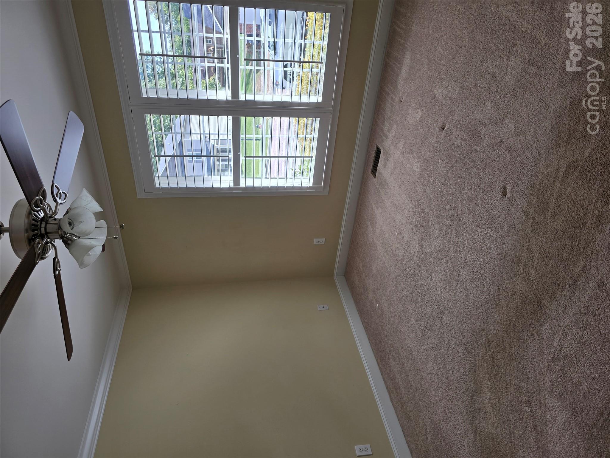 Empty bedroom with carpet, a ceiling fan, and large plantation-shuttered windows.