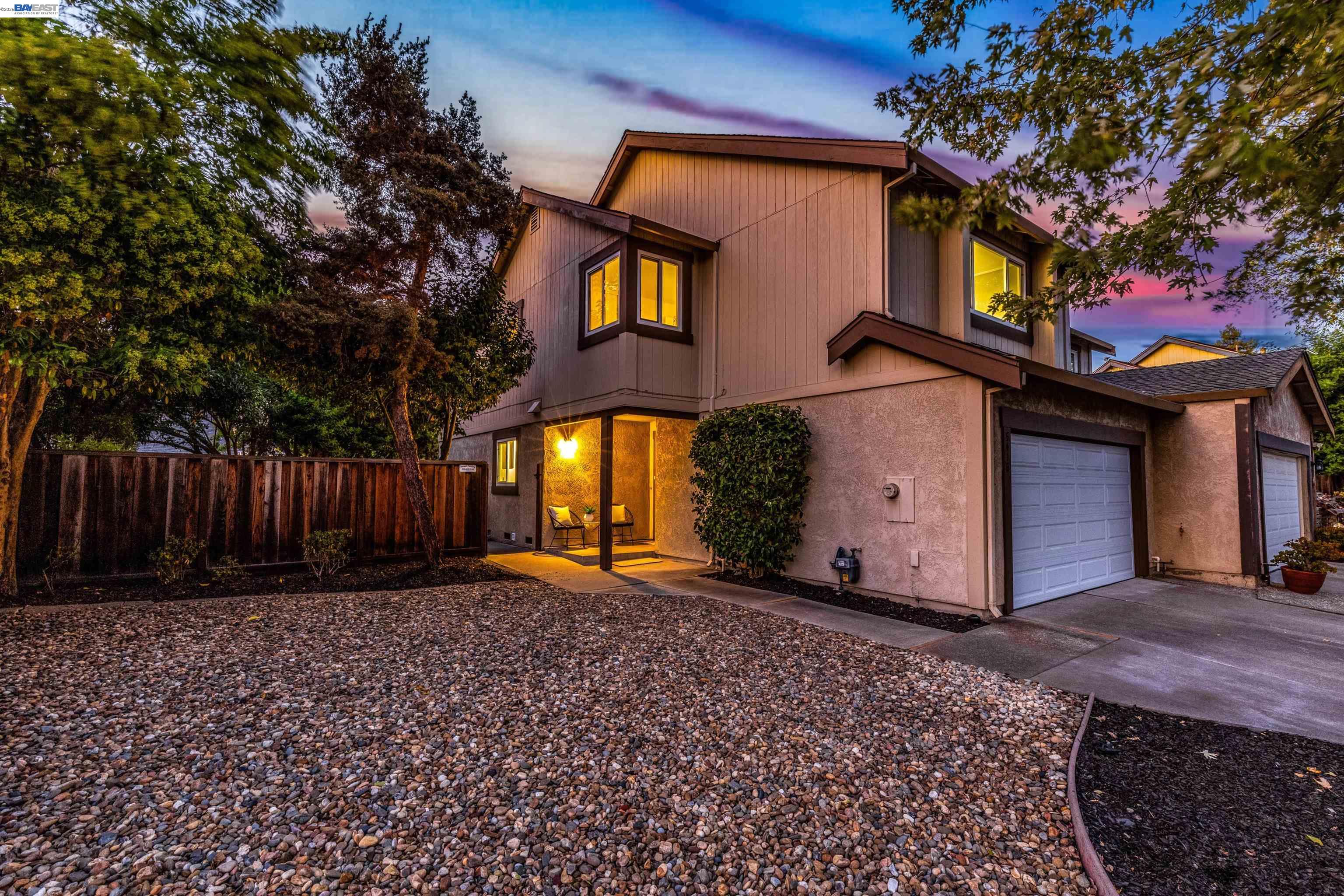 Two-story home at dusk with glowing windows, a covered entry, gravel landscaping, and two garages.