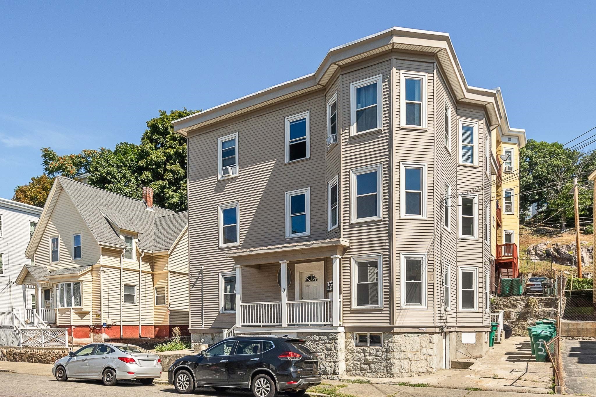 Multi-story beige-sided home with an angled bay facade, covered porch, and stone foundation.