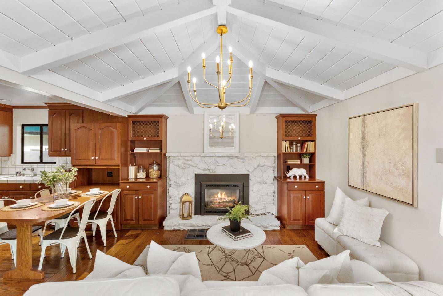 Living and dining room with a vaulted white ceiling, stone fireplace, wood built-ins, and white seating.