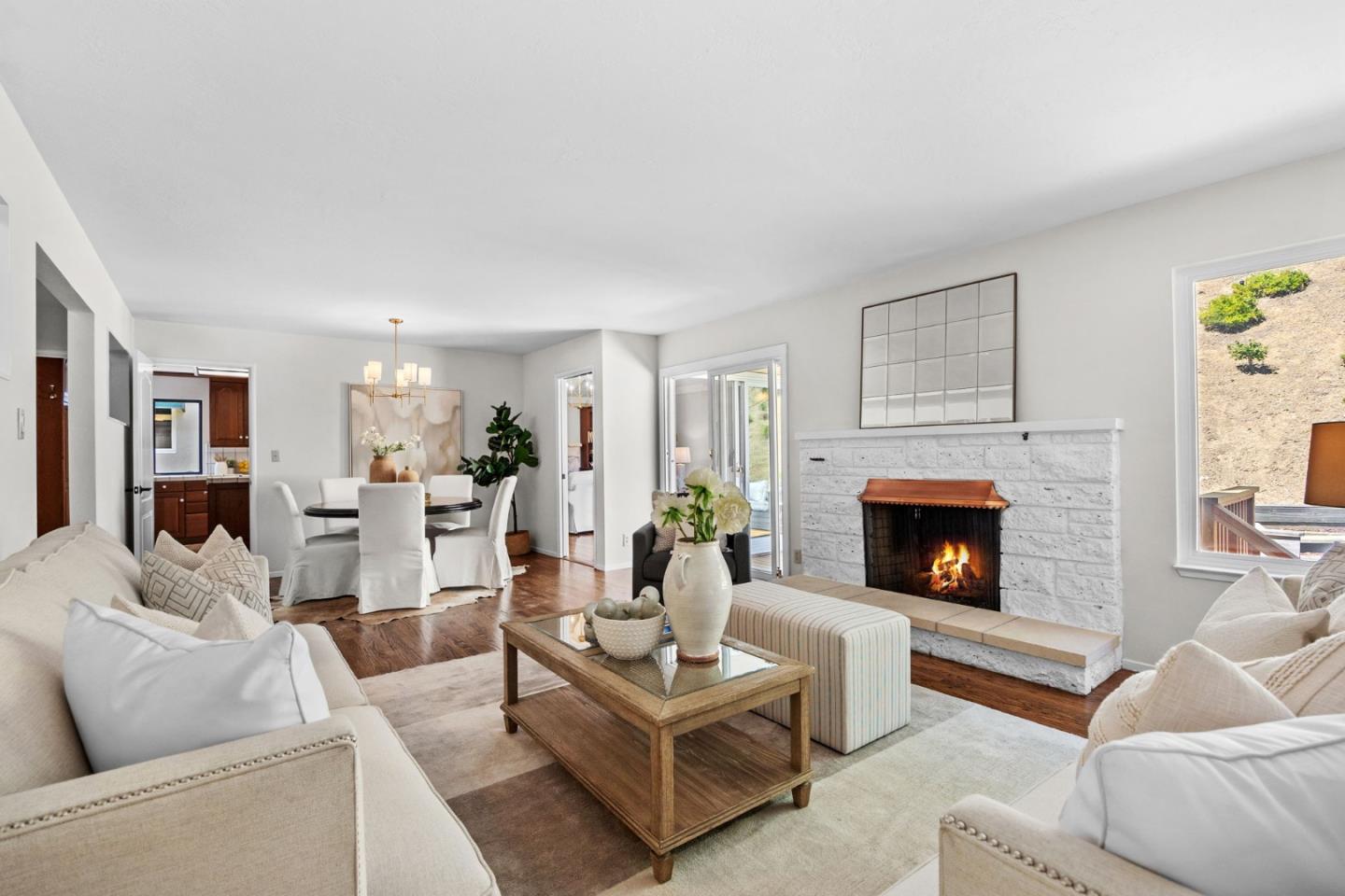 Living room with a white stone fireplace, light sofas, hardwood floors, and an adjoining dining area.