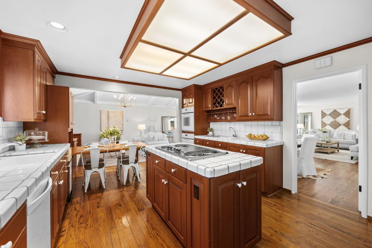 Kitchen with warm wood cabinetry, white tile counters, and a large cooktop island beside a dining area.