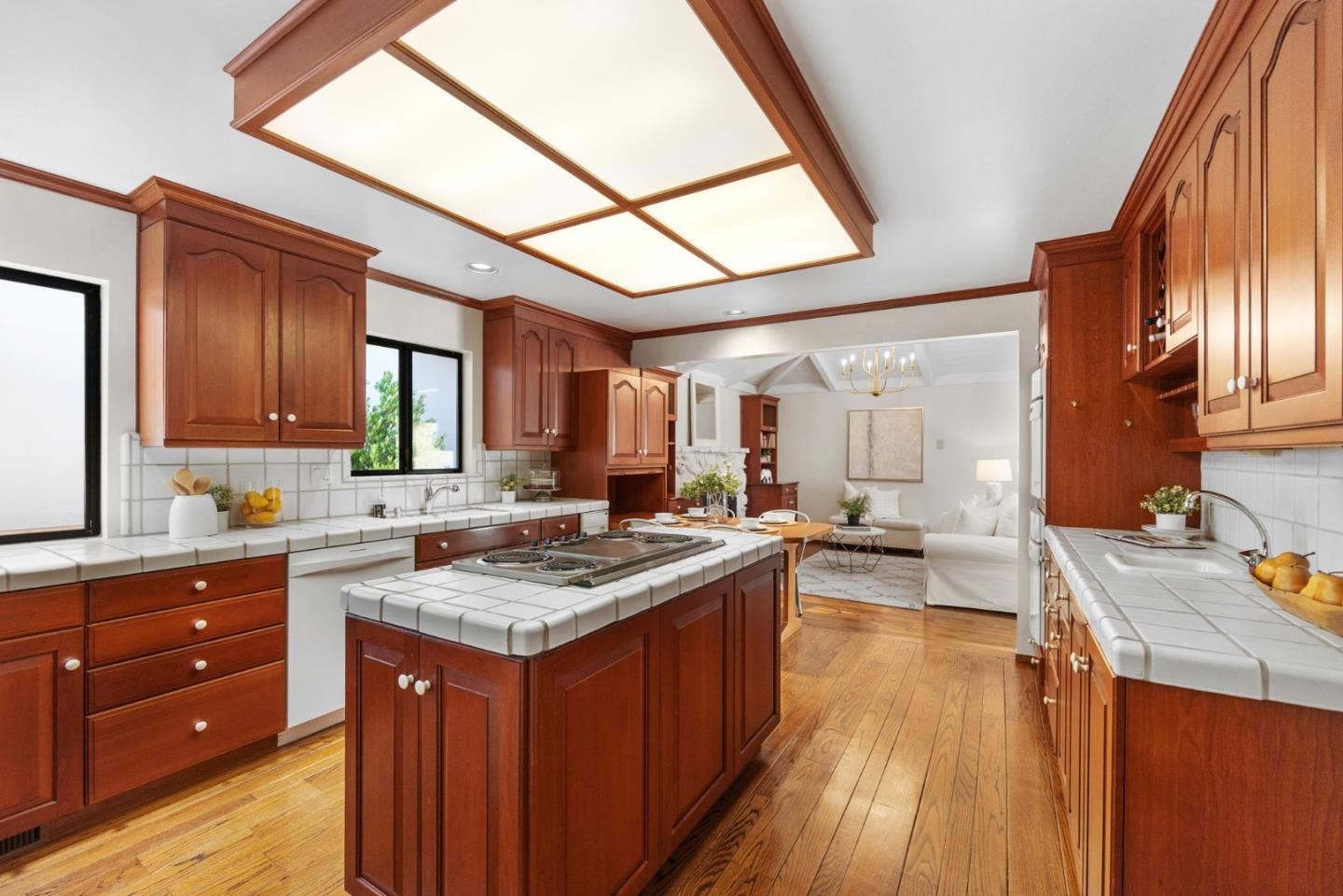 Kitchen with reddish wood cabinetry, tiled counters, a large cooktop island, and an adjoining sitting area.