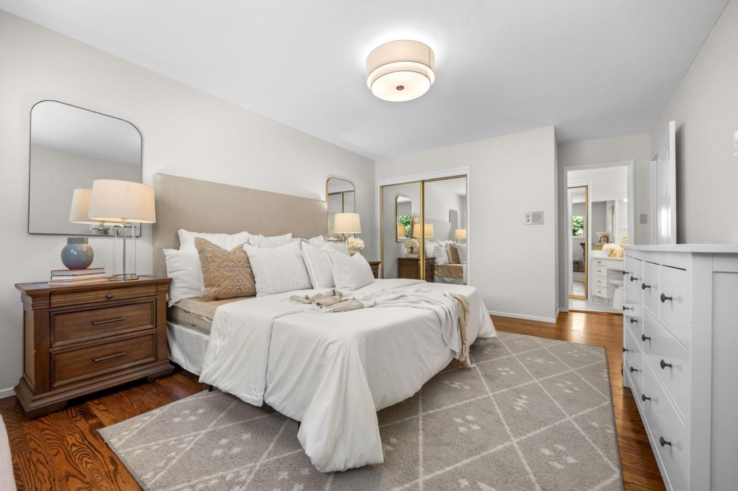 Staged bedroom with a white bed, mirrored closet doors, and a gray patterned rug.