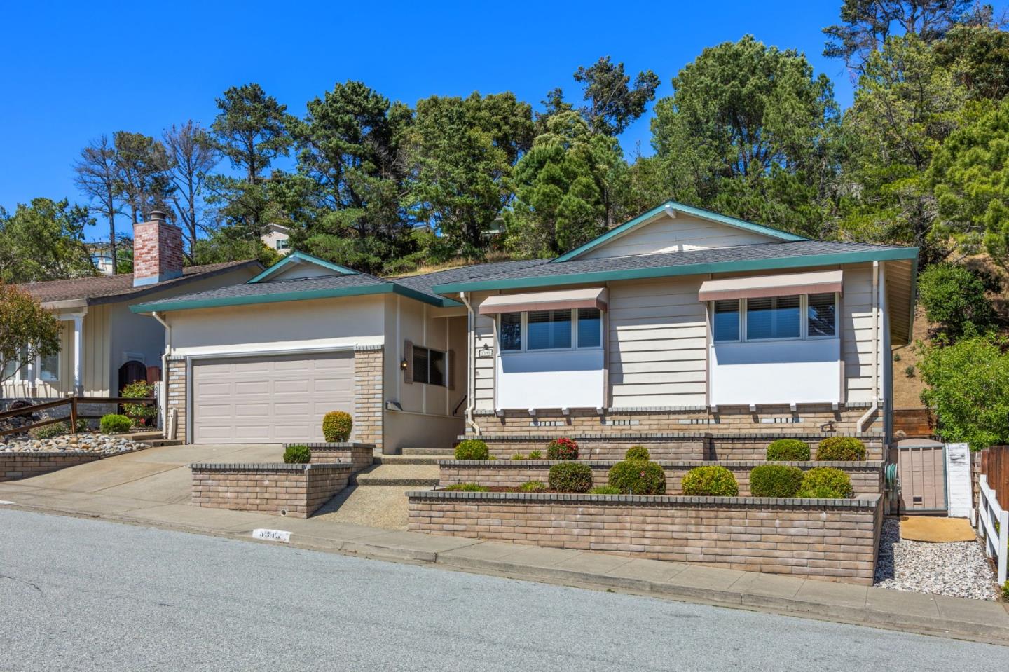 Single-story home with teal roof trim, two-car garage, and terraced brick landscaping.