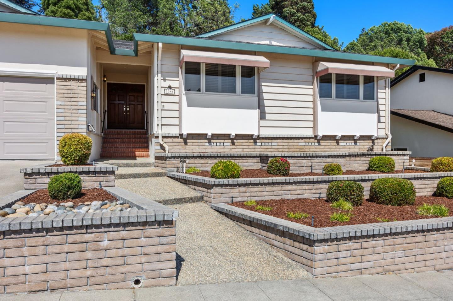 Home exterior with green roof trim, tiered brick planters, and a walkway to the recessed front door.