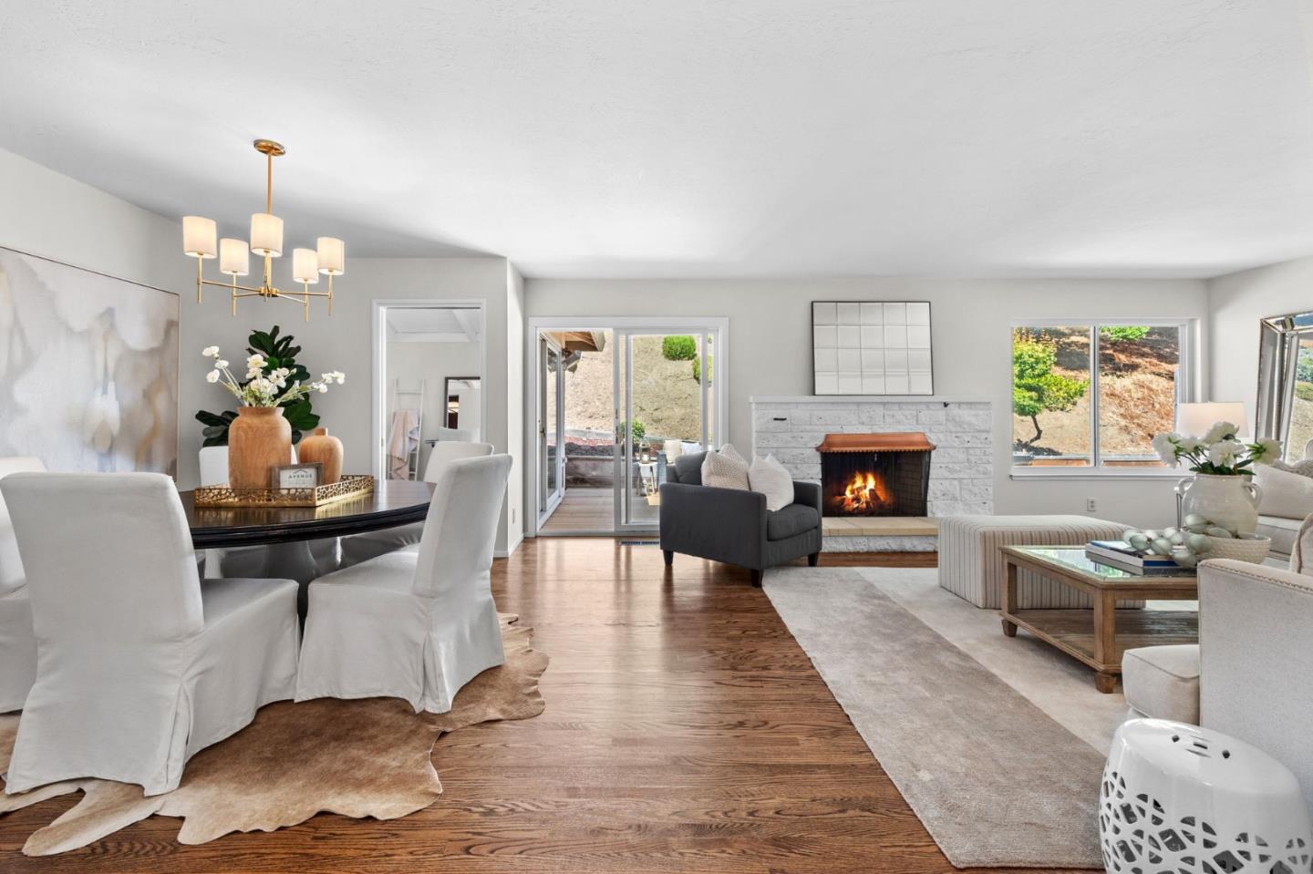 Open-plan living and dining room with hardwood floors and a white stone fireplace.