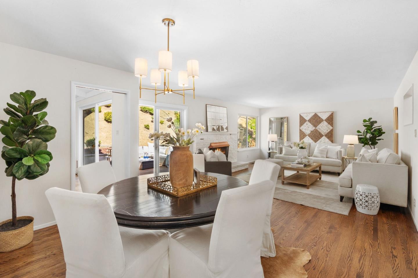 Open-plan dining and living room with a fireplace, white furnishings, and warm wood floors.