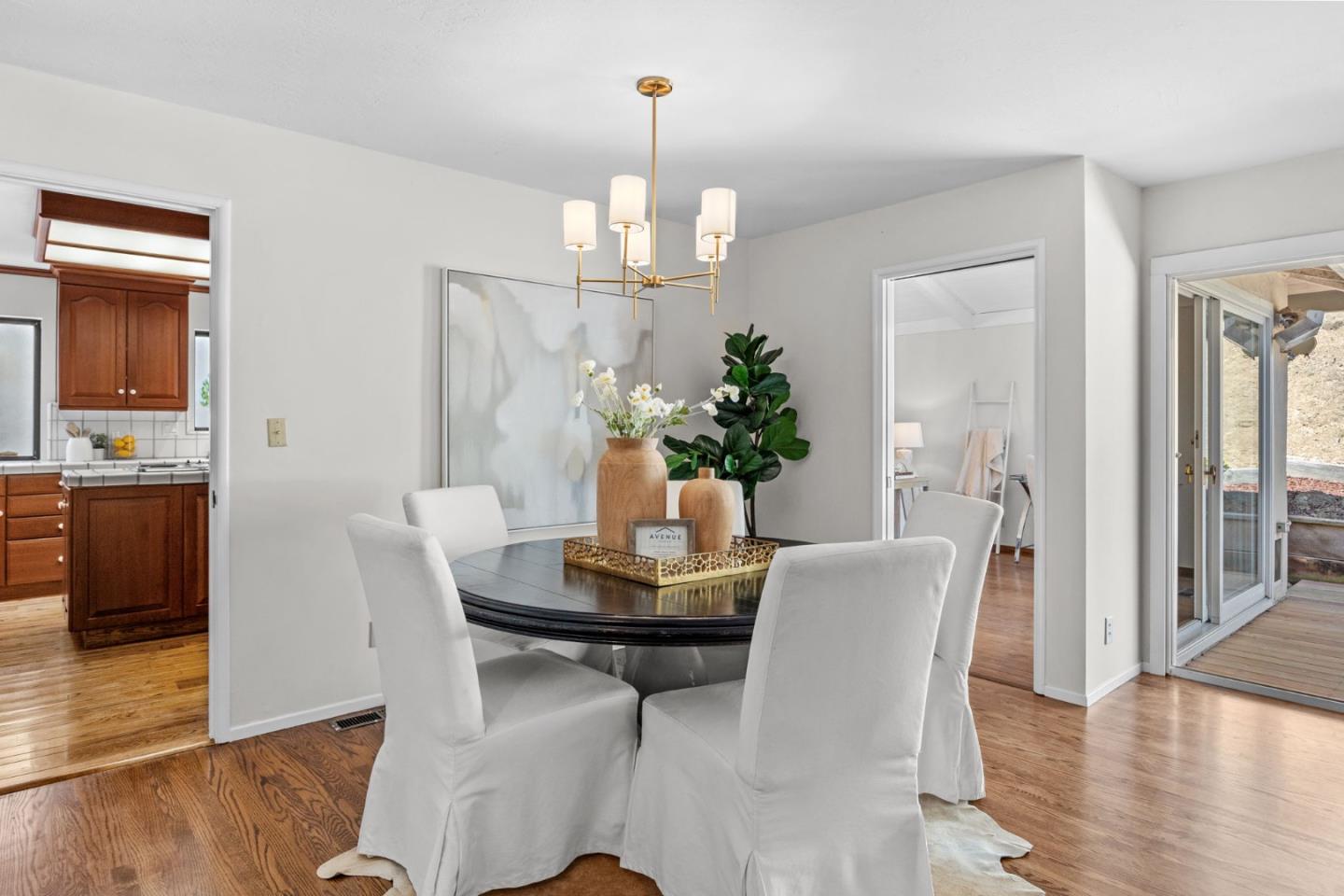 Staged dining room with a round table, white chairs, brass chandelier, and sliding glass doors.