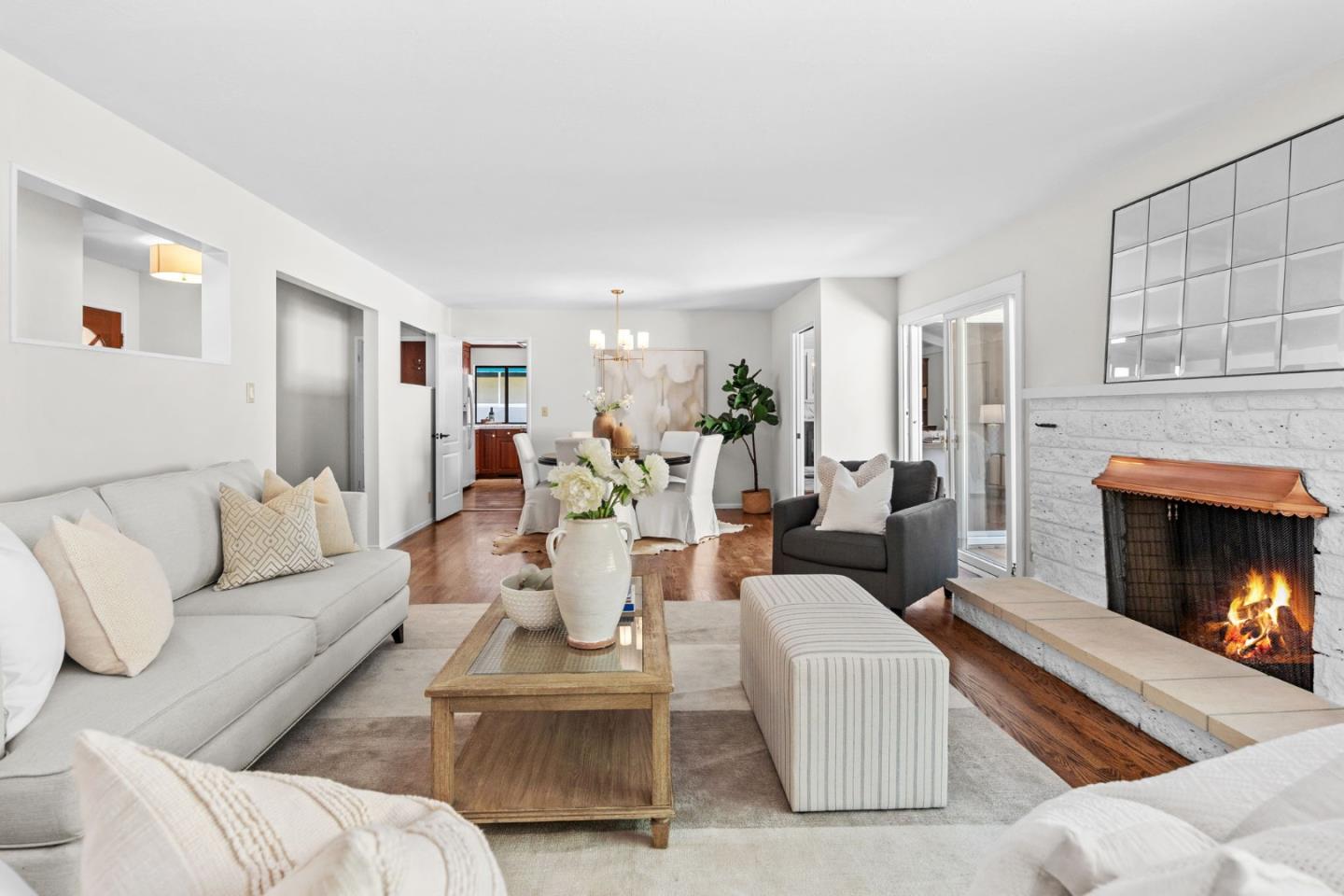 Staged living room with a stone fireplace, hardwood floors, and an open dining area.