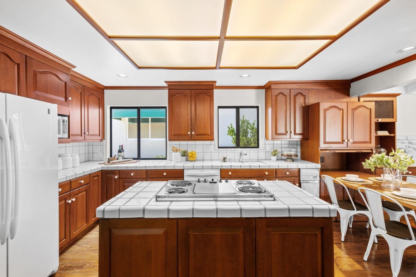 Kitchen with warm wood cabinets, a tiled island cooktop, and a wood-framed ceiling panel.