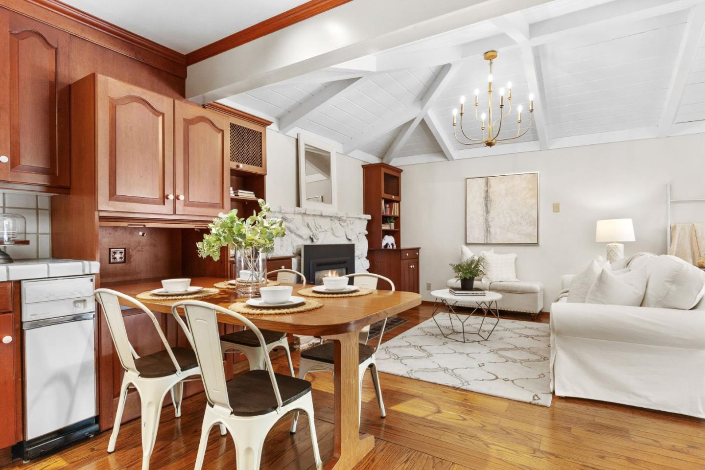 Open kitchen and living area with wood cabinetry, a stone fireplace, and a vaulted beamed ceiling.