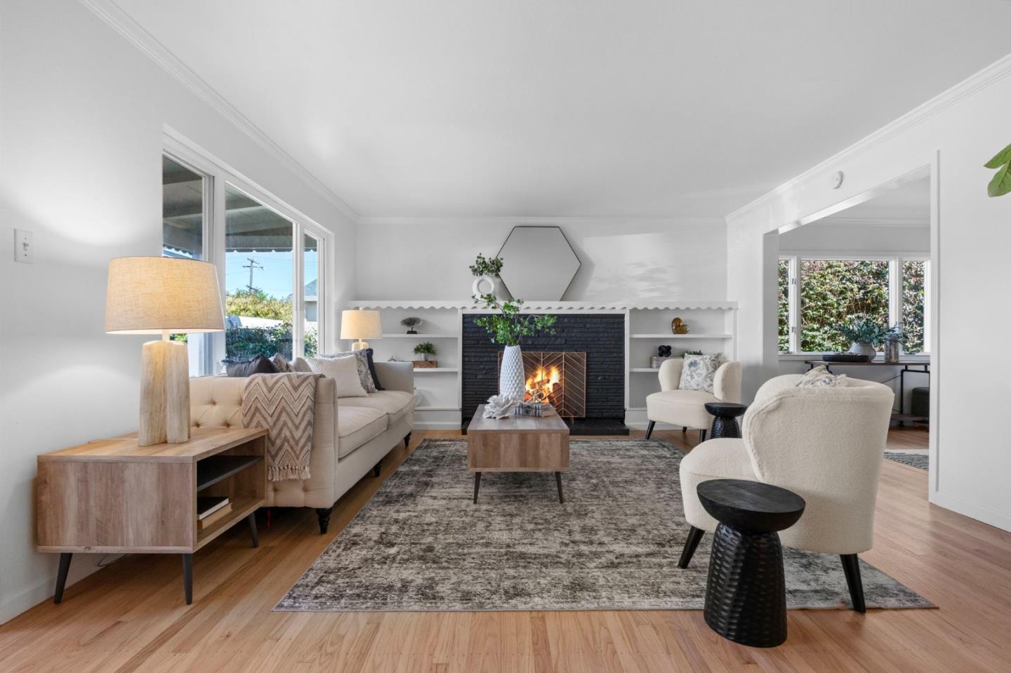 Staged living room with a black brick fireplace, built-in shelves, cream seating, and hardwood floors.