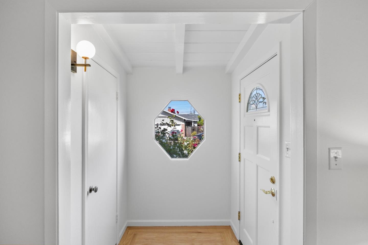 Bright entryway with exposed ceiling beams, hardwood flooring, and an octagonal window overlooking a garden.