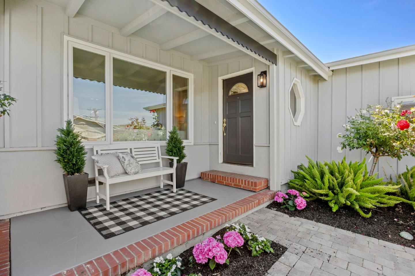 Home's front porch with a dark door, white bench, brick steps, and pink flowers.
