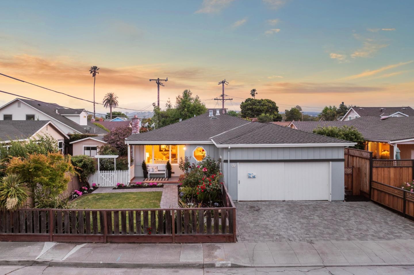 Home exterior with a wide paver driveway, attached garage, and landscaped yard at dusk.
