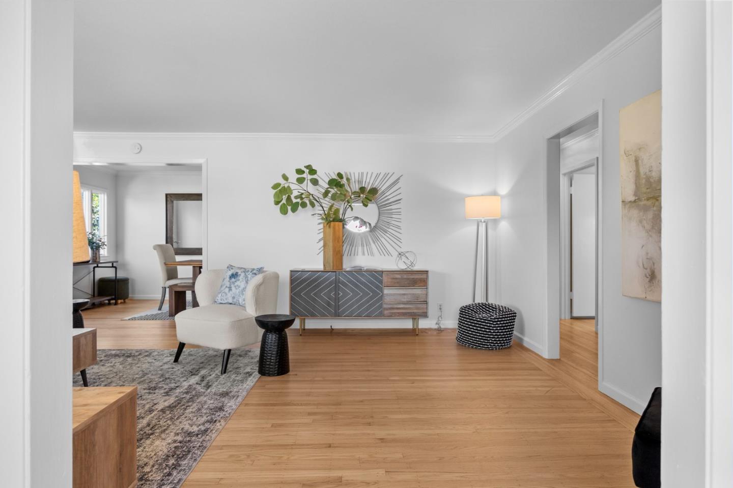 Staged living room with a cream chair, patterned sideboard, and light wood floors.